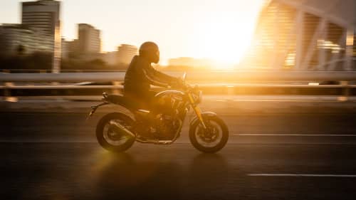 Man riding Triumph Speed 400 down a road with a sunset in the background