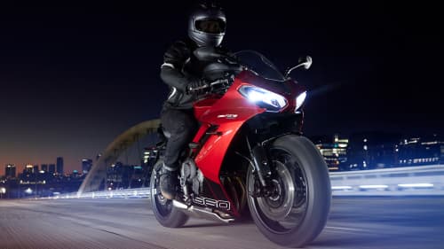 Triumph Daytona 660 in carnival red and sapphire black riding through city at night