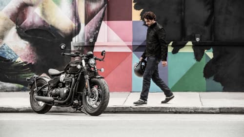 Triumph Bonneville Bobber Black parked on street with mural in background