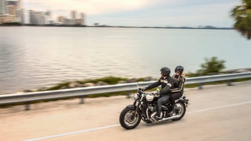Triumph Speedmaster with rider and pillion riding along Miami coast
