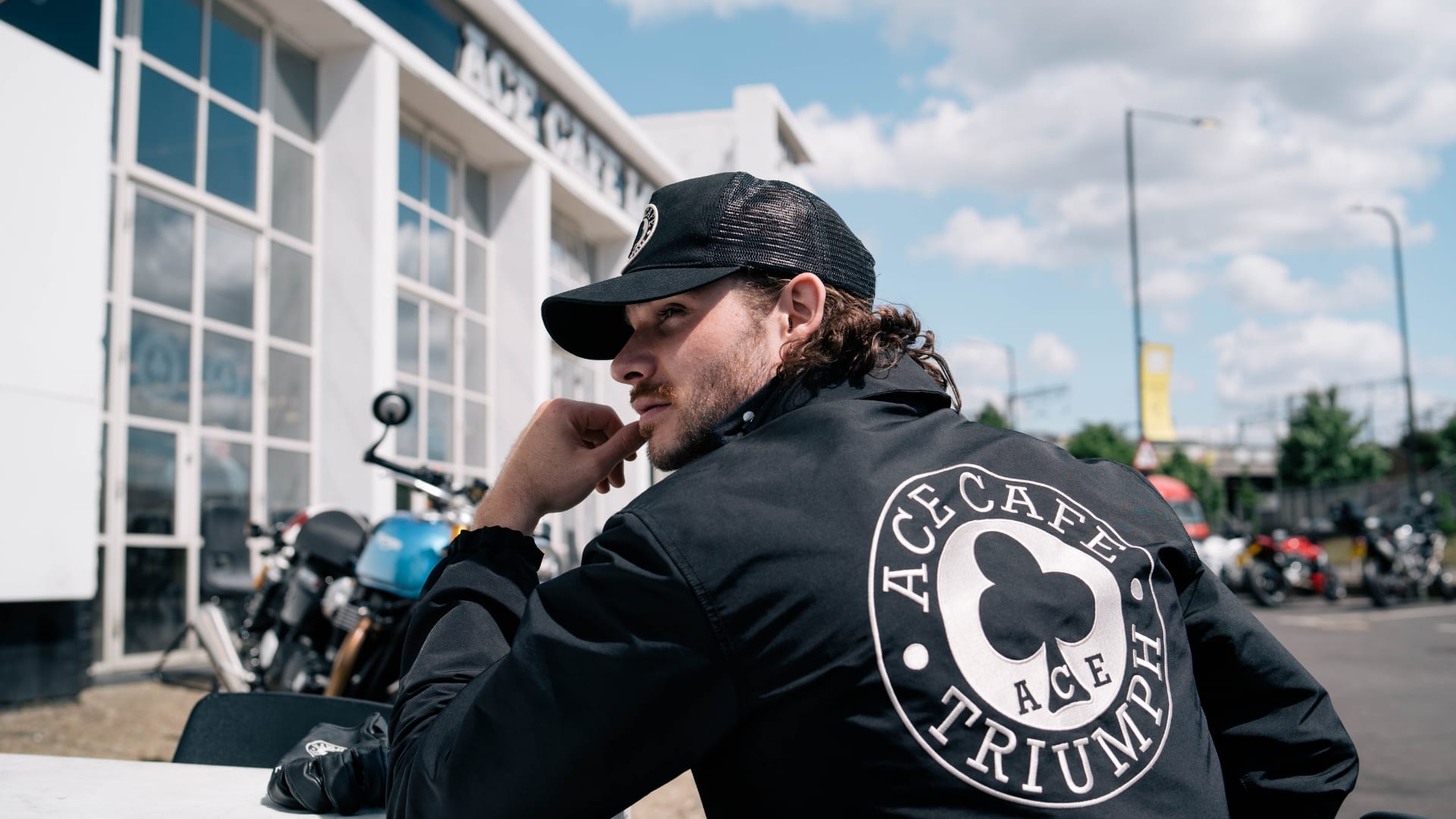 Man sitting at table outside with Triumph Ace Cafe Shirt and Cap