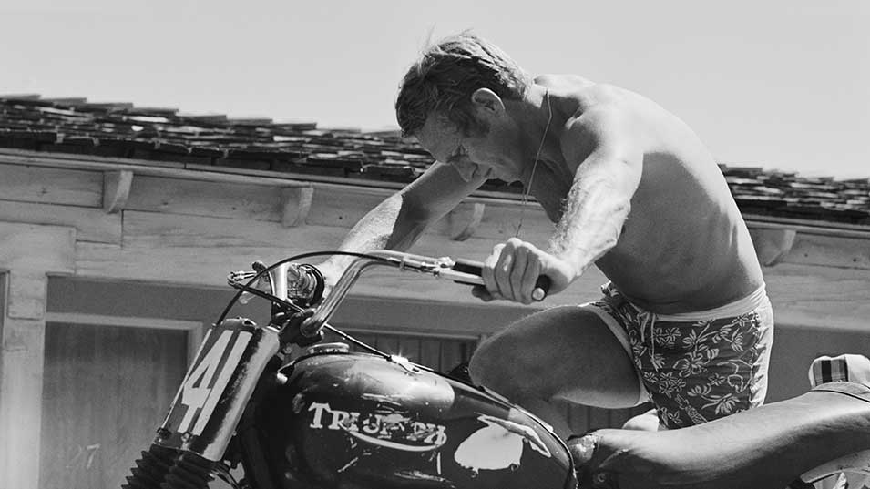Steve McQueen pushing an iconic Triumph Motorcycle