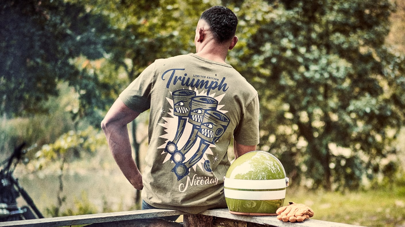 Man sitting on fence with helmet wearing Triumph Lifestyle Triple Graphic Tee