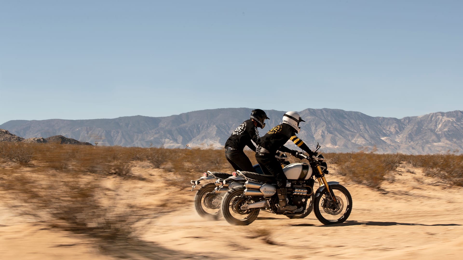 Two Triumph Scrambler 1200s scrambling across the dessert in extreme off-road style