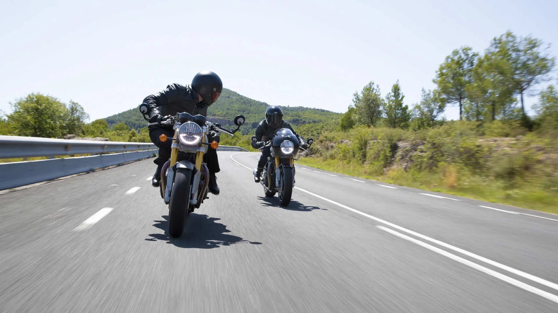 Front shot of two Triumph Thruxton RS motorcycles riding down a straight road