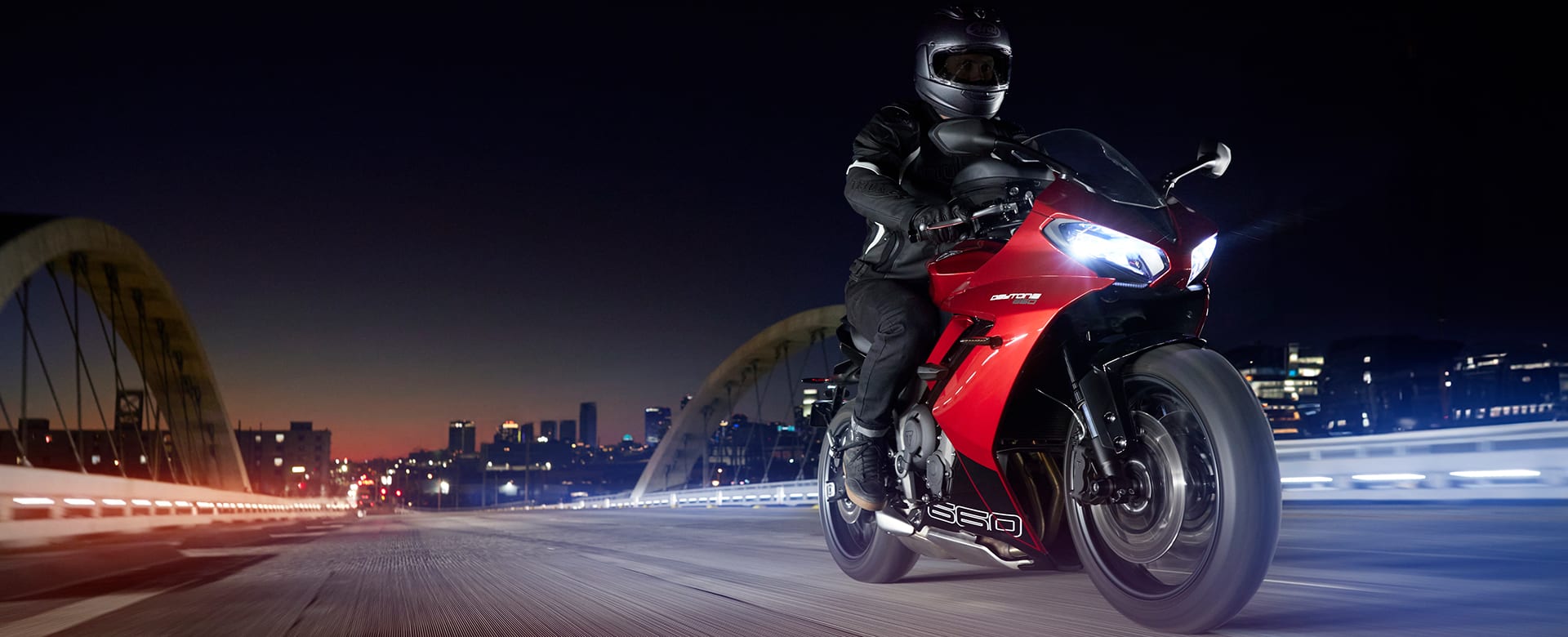 Triumph Daytona 660 in carnival red and sapphire black riding through city at night