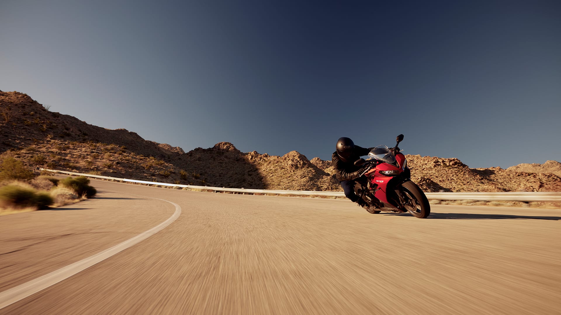 Triumph Daytona 660 in carnival red and sapphire black riding on mountain road)