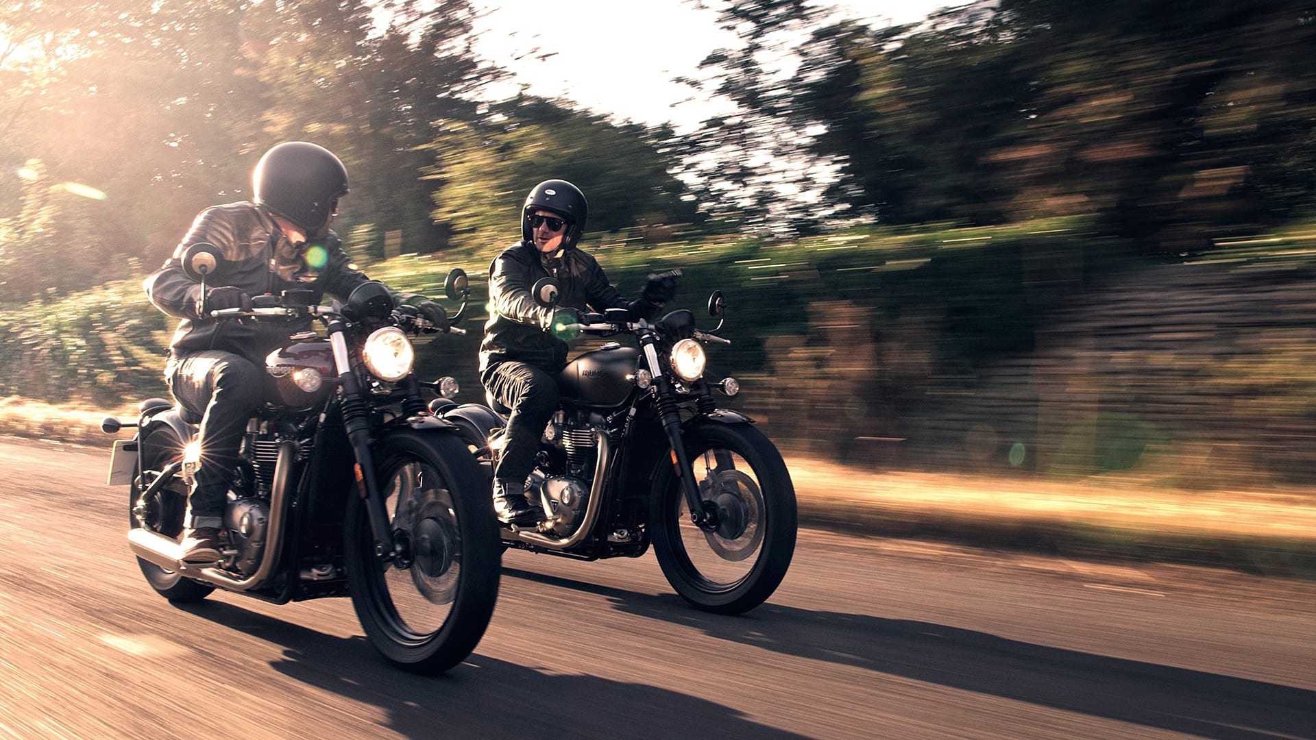 Two riders riding Triumph Bobbers next to one another through street