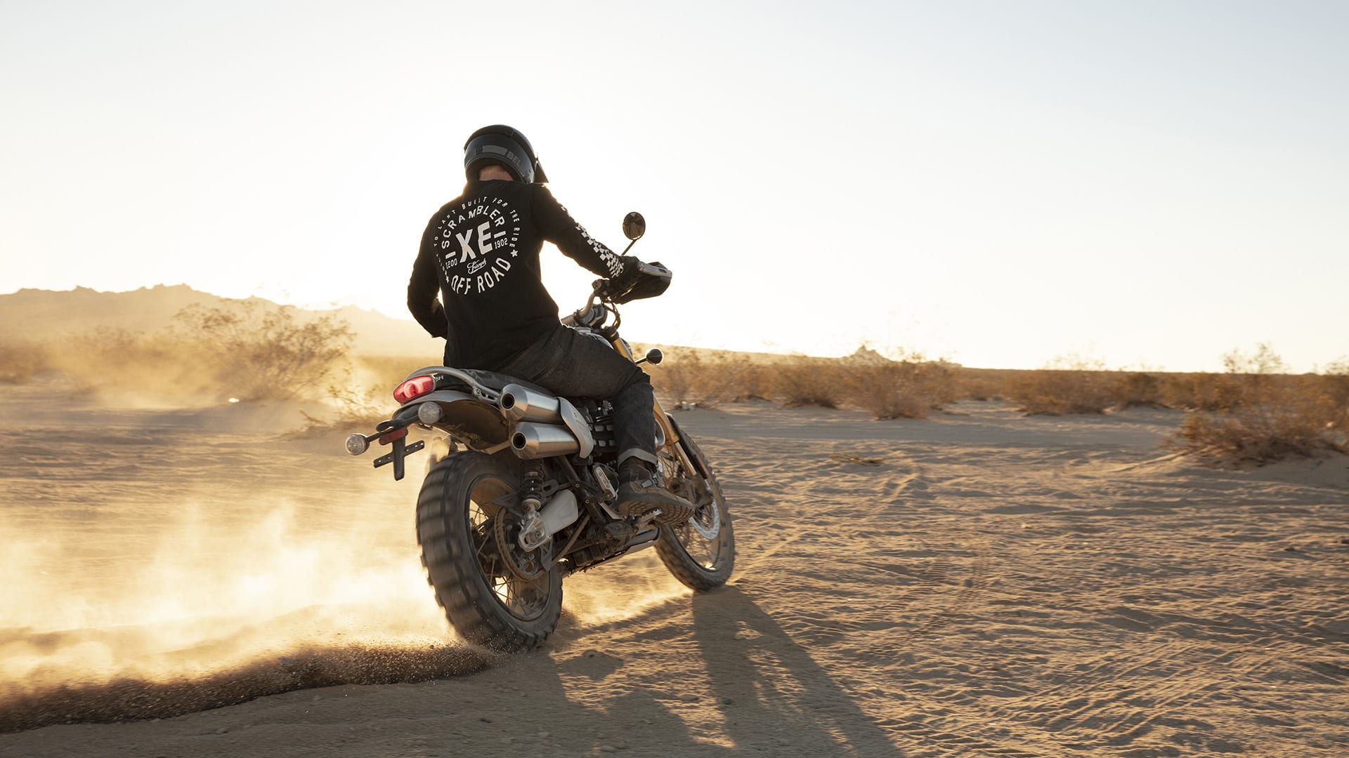 Innovative Triumph Scrambler 1200 scrambling along a salt flat in thrilling style, with the rider wearing the limited edition Scrambler 1200 clothing collection and Triumph dirt boots