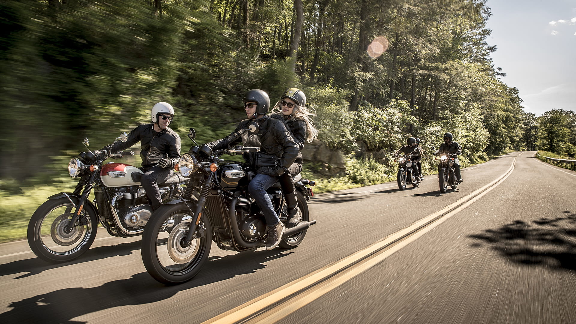 Group of four riders on Triumph T100 riding through country roads