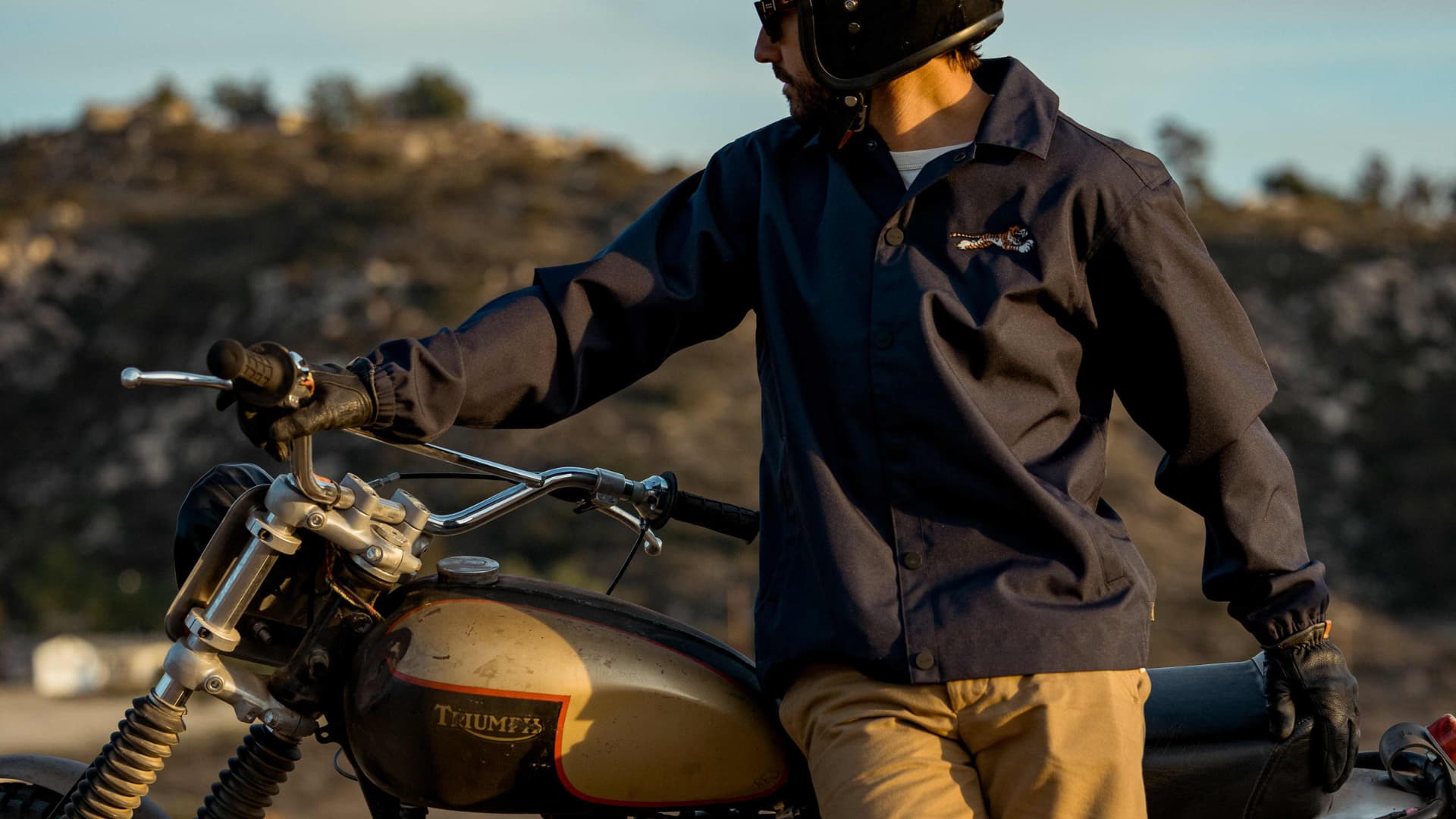 An image of a rider leaning against a Triumph Motorcycle wearing Triumph Heritage clothing.