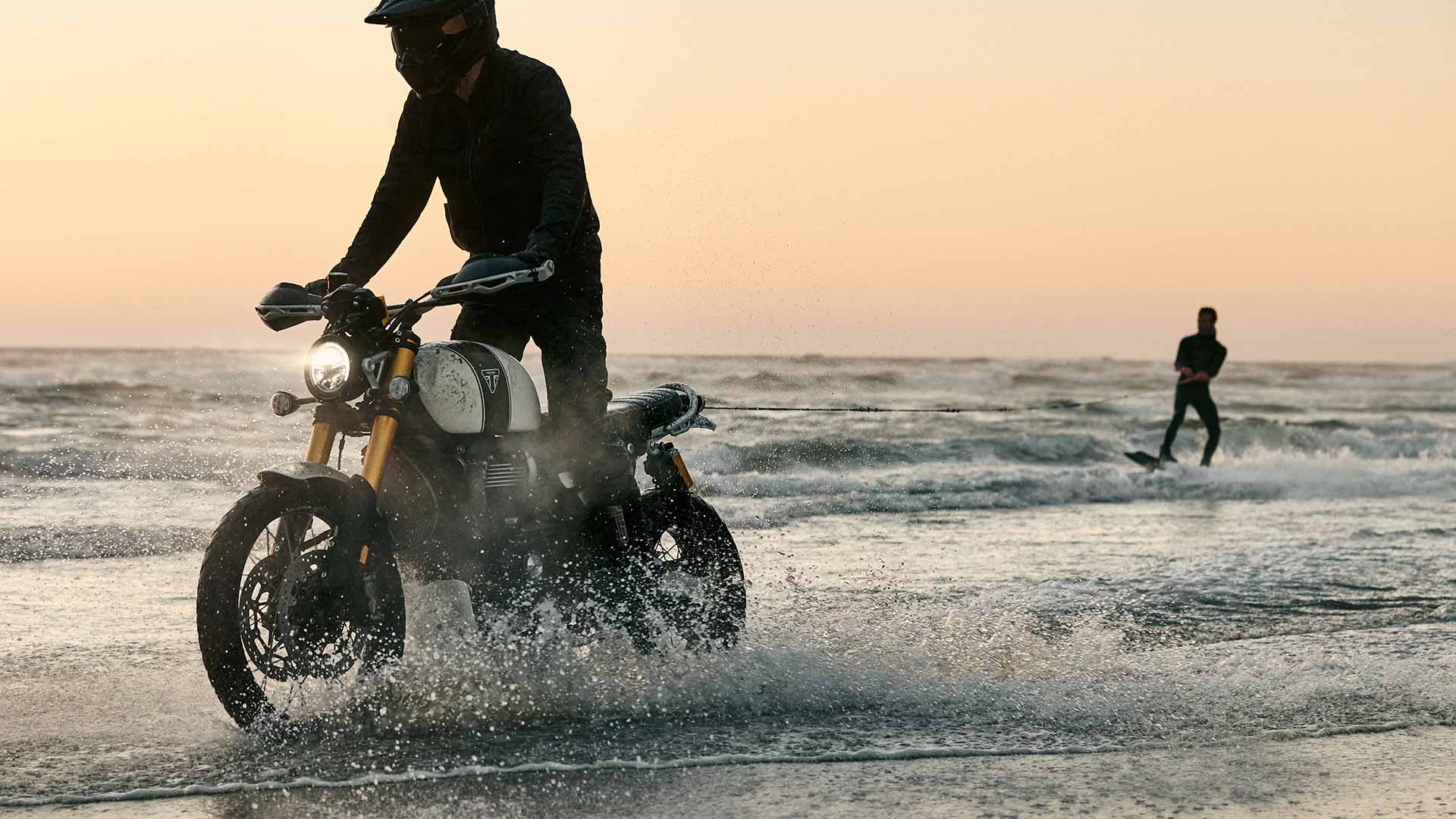 Triumph Scrambler 1200 XE being ridden through waves on a beach towing a wakeboarder