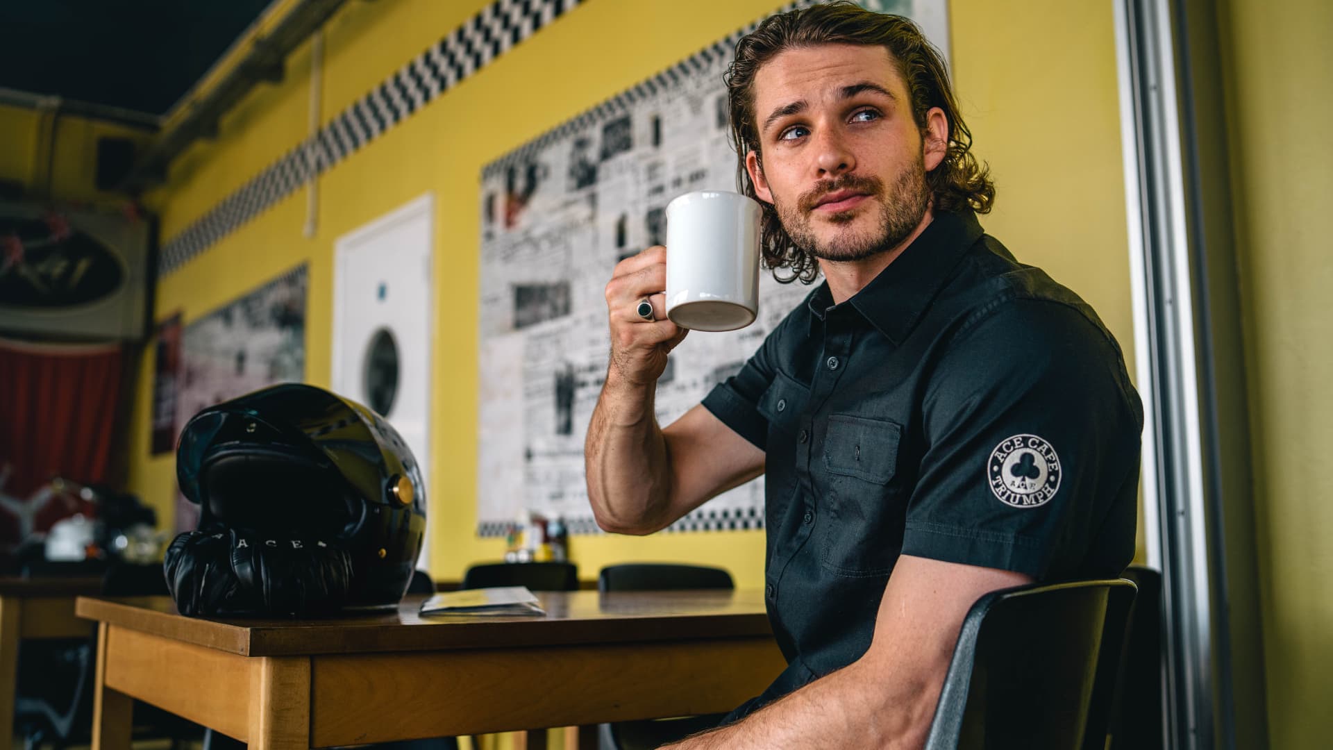 Man in Ace Cafe drinking tea wearing Triumph shirt