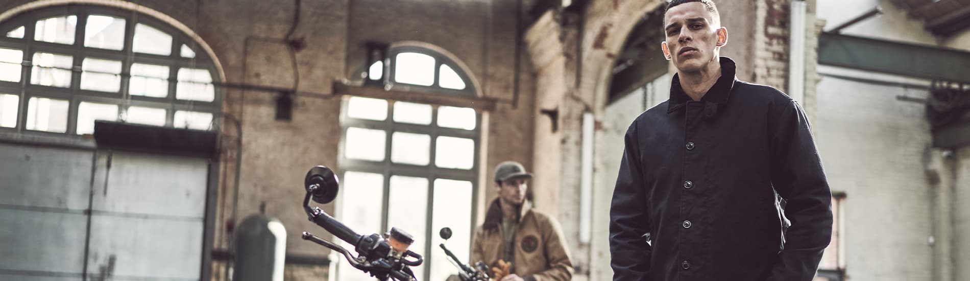 A man in a blue Triumph jacket stood next to a Triumph motorcycle)