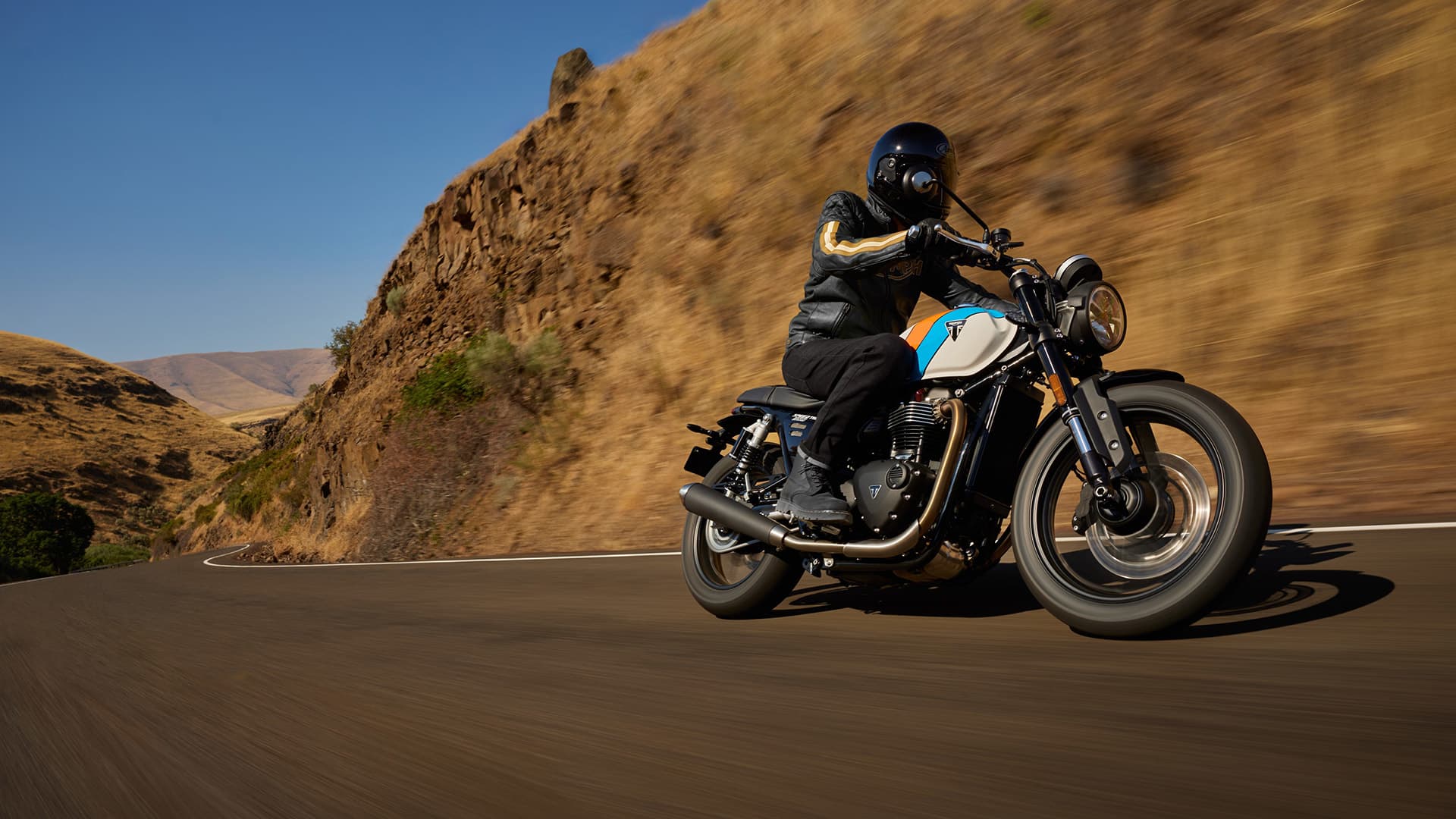 Rider on Triumph Speed Twin 900 riding past hills on a road