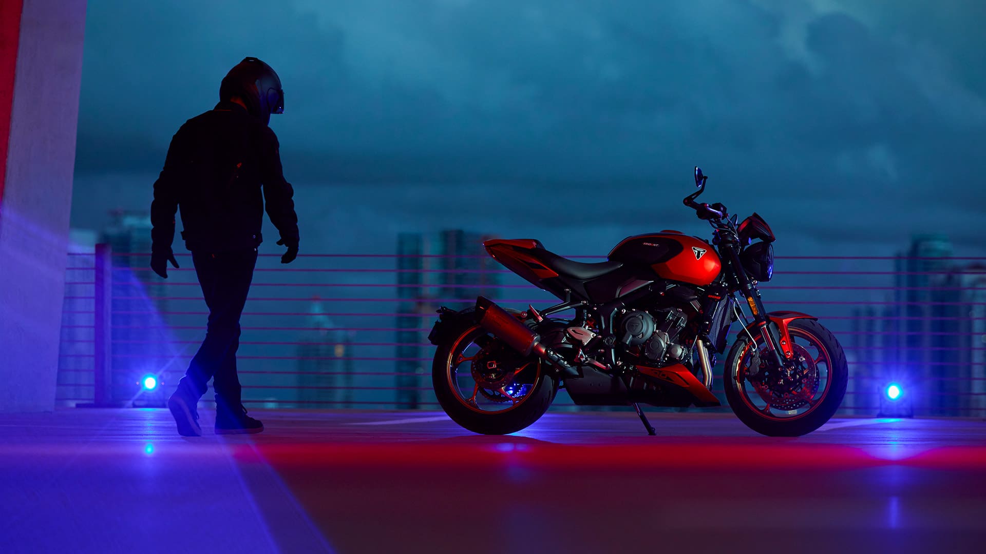 Side shot of a rider walking toward stationary Triumph Trident 800 in Carnival Red