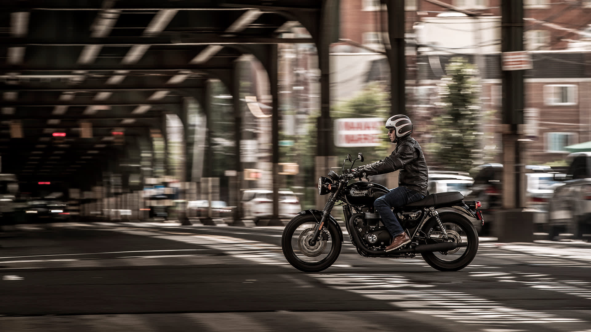 Triumph Bonneville T100 Black riding underneath a bridge  in an urban area