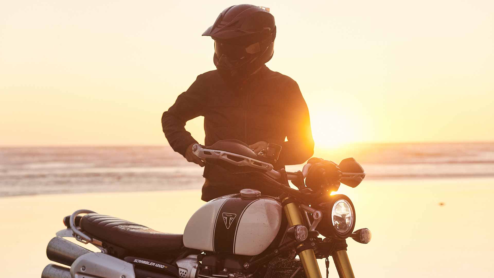 Triumph Scrambler 1200 XE with rider stood beside at sunset