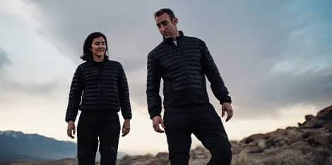 a man and woman walking down a hill at dusk wearing down jackets