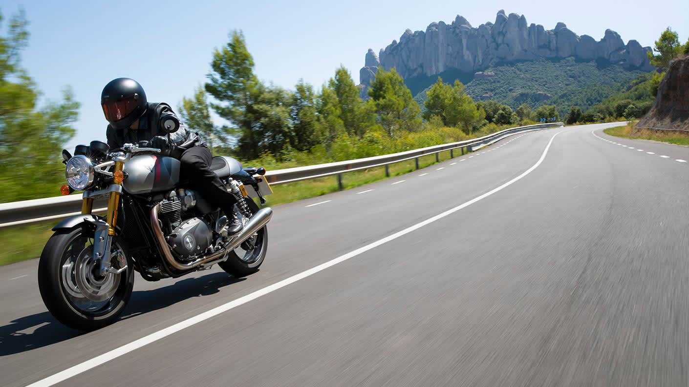 Action shot of rider accelerating through scenic mountainous roads on the new Triumph Thruxton RS