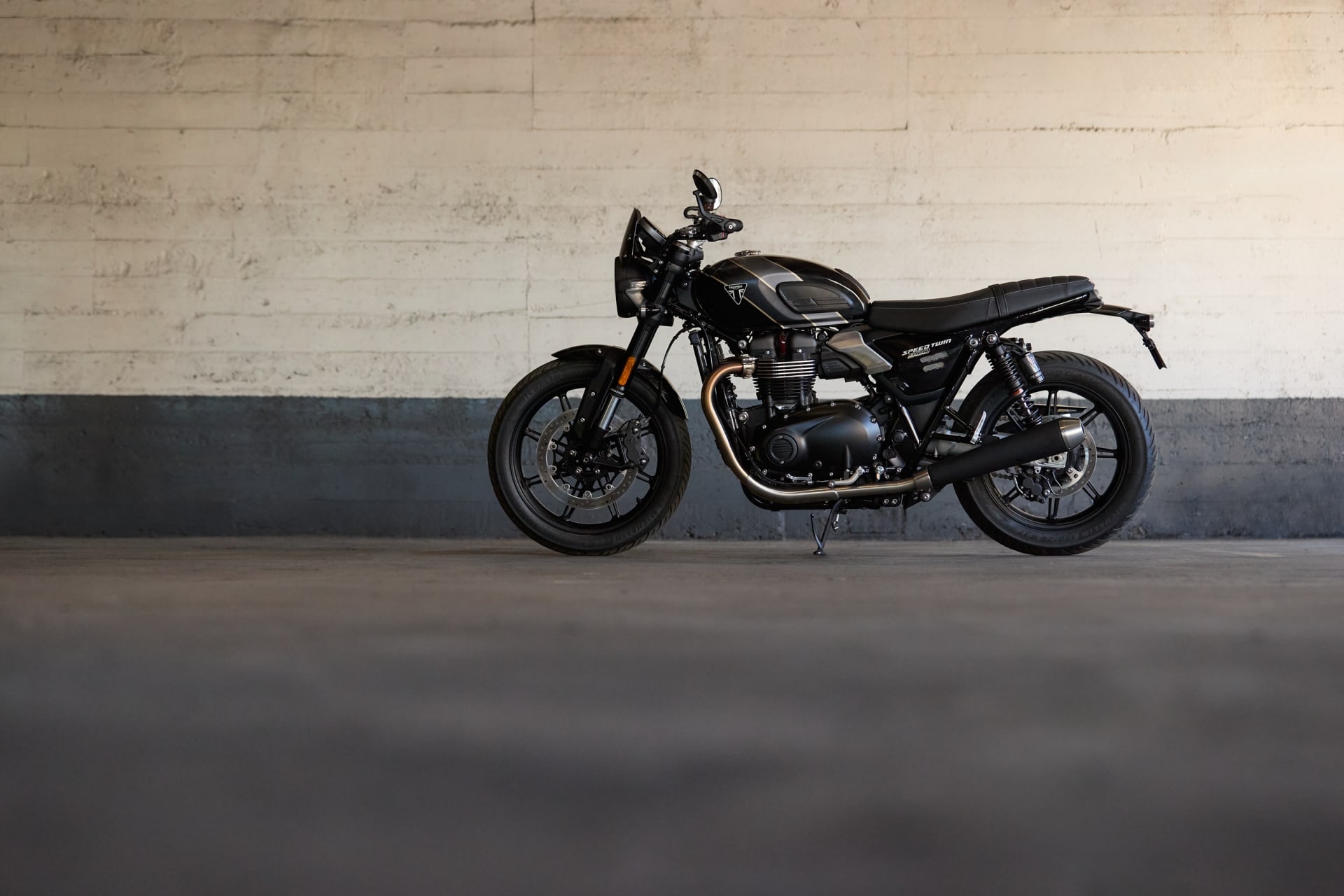 Side profile of a black Speed Twin 900 motorcycle parked against a concrete wall.