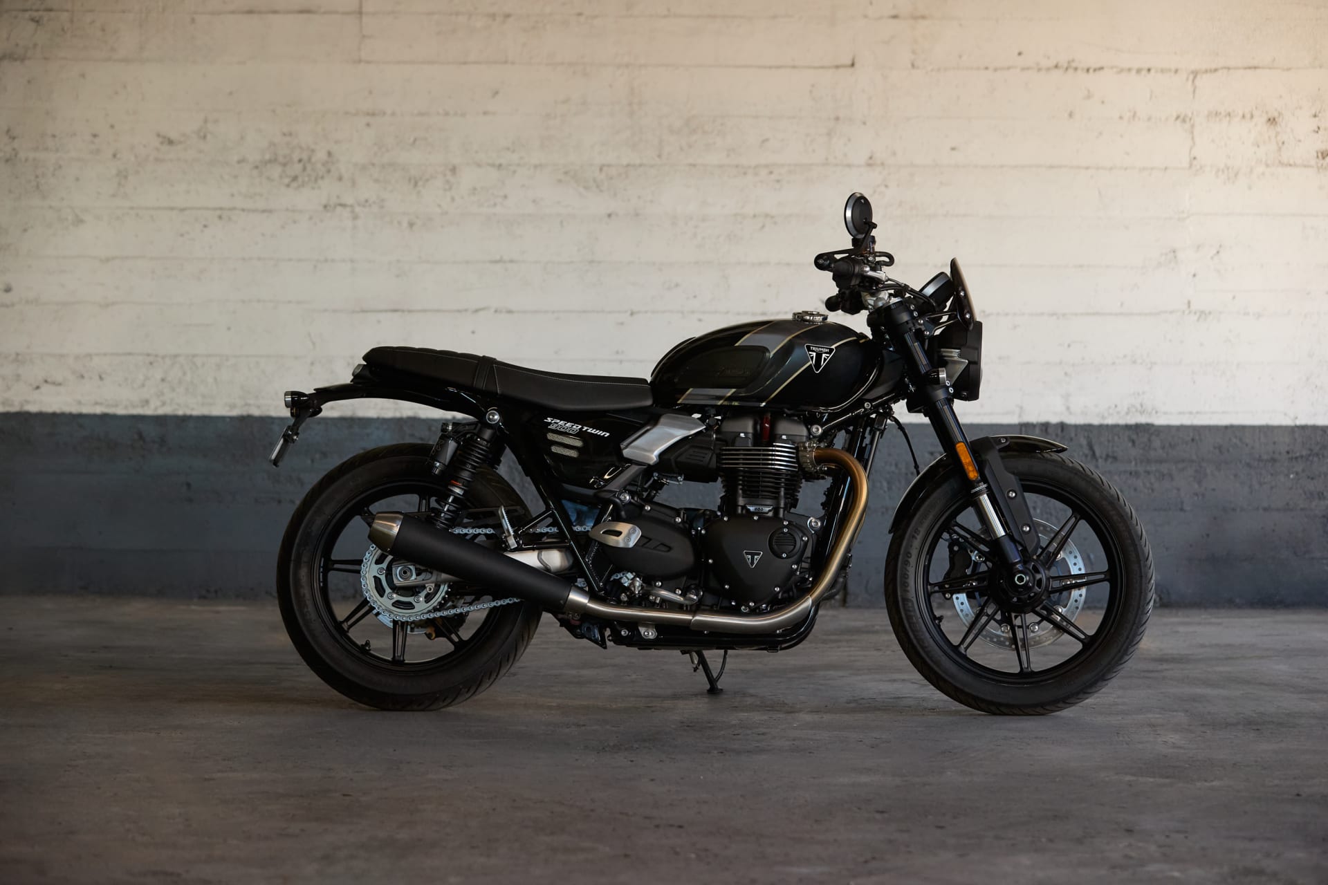 Side profile of a black Speed Twin 900 motorcycle parked against a concrete wall