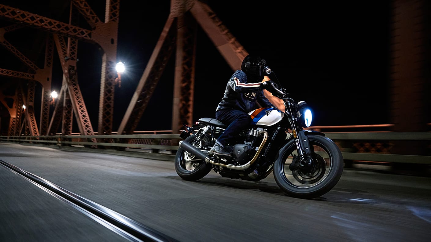 ΠΡΟΣΑΡΜΟΣΙΜΗ ΑΠΟΔΟΣΗ Right side view of a rider on Triumph Speed Twin 900 on a bridge at night
