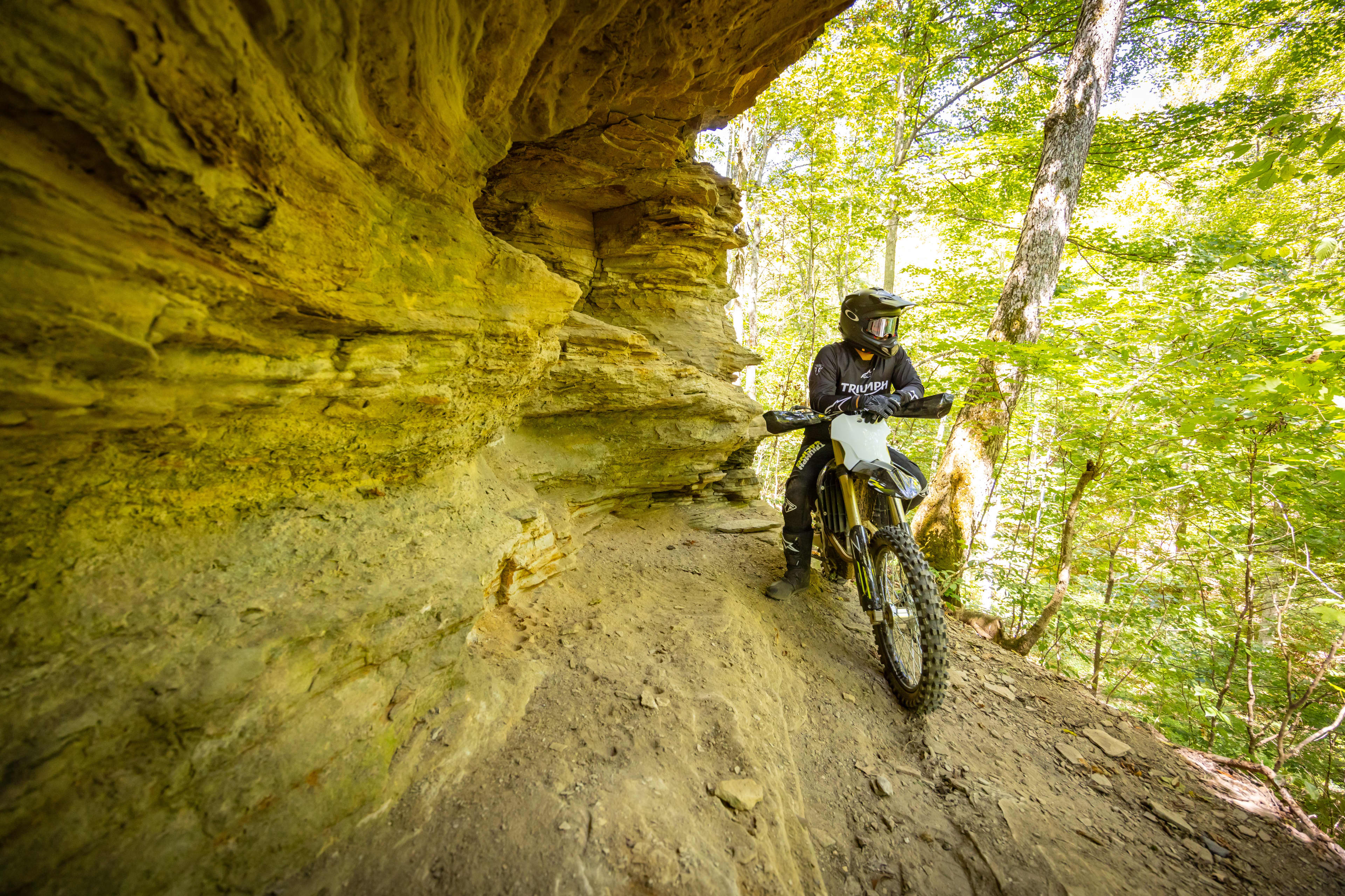 Triumph Cross Country motorcycle admiring the forest under a cliffside