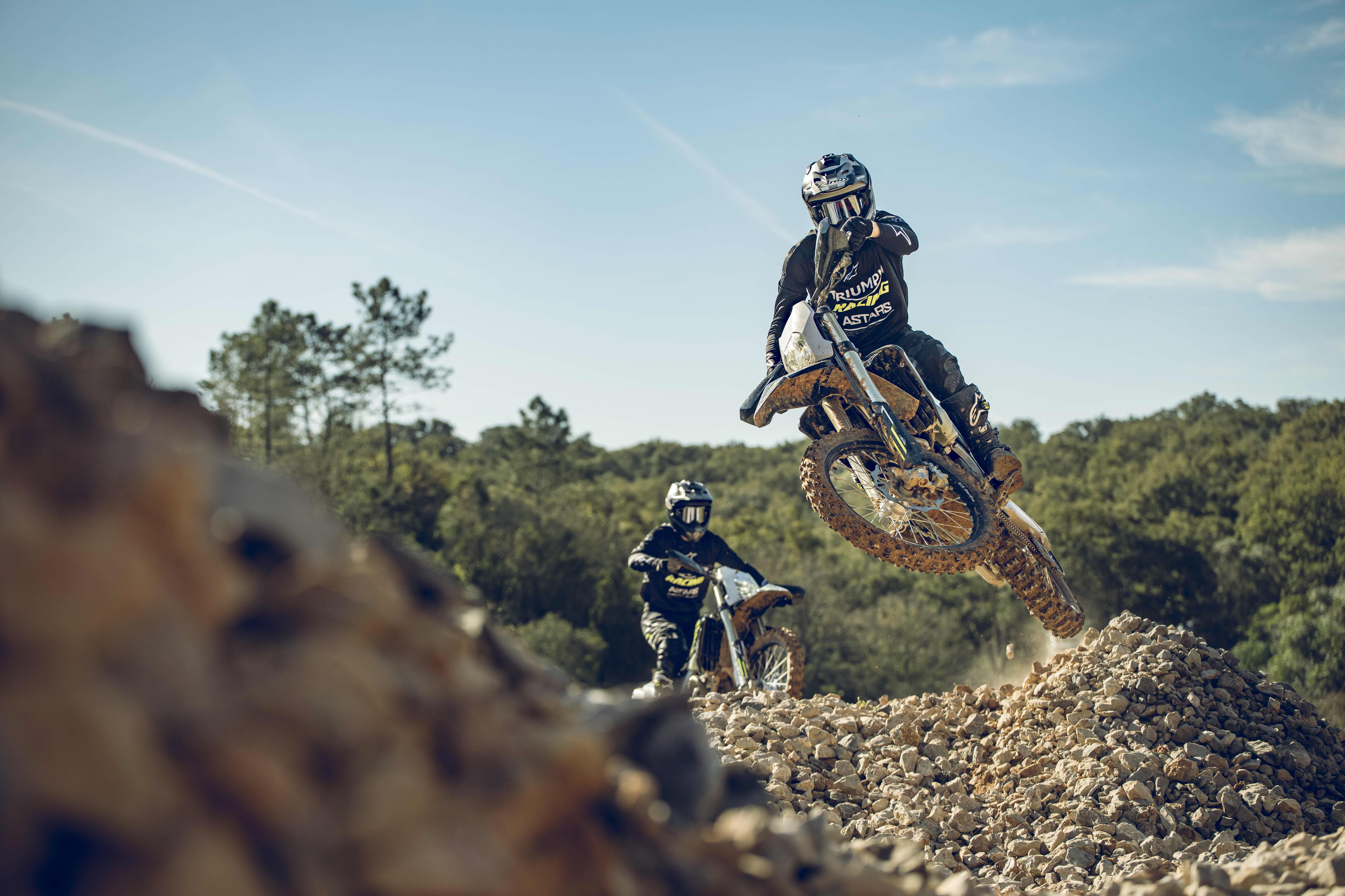 Enduro Action shot of a motocross rider in full protective gear jumping a Triumph TF 250-E Enduro bike over a rocky dirt embankment followed by a rider on a TF 450-E.
