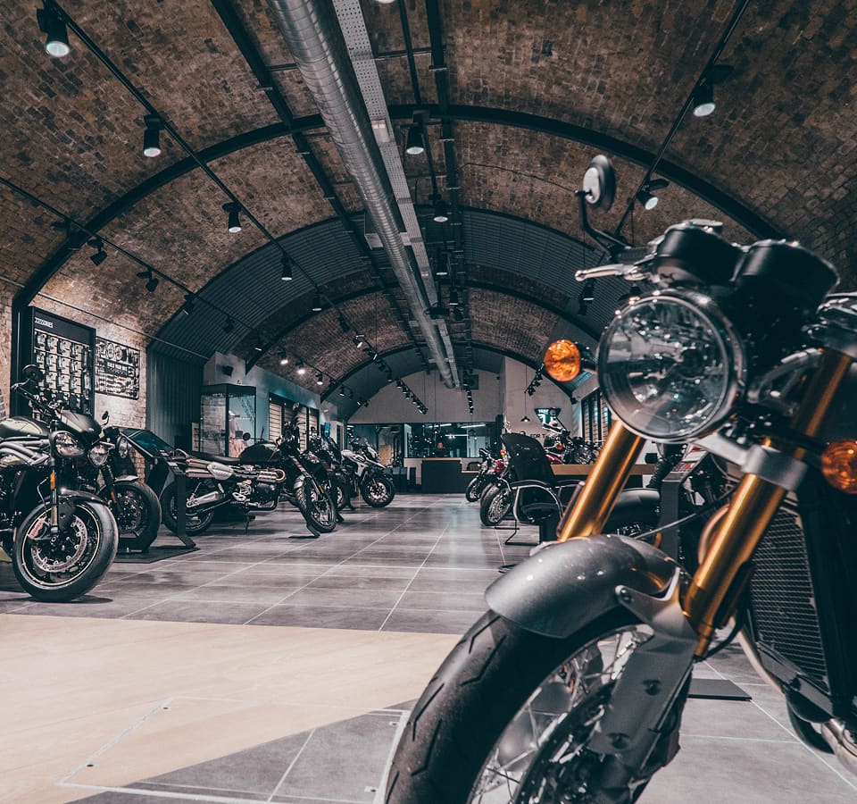 A motorcycle showroom under arched brick ceilings with several Triumph motorcycles parked along a tiled aisle.