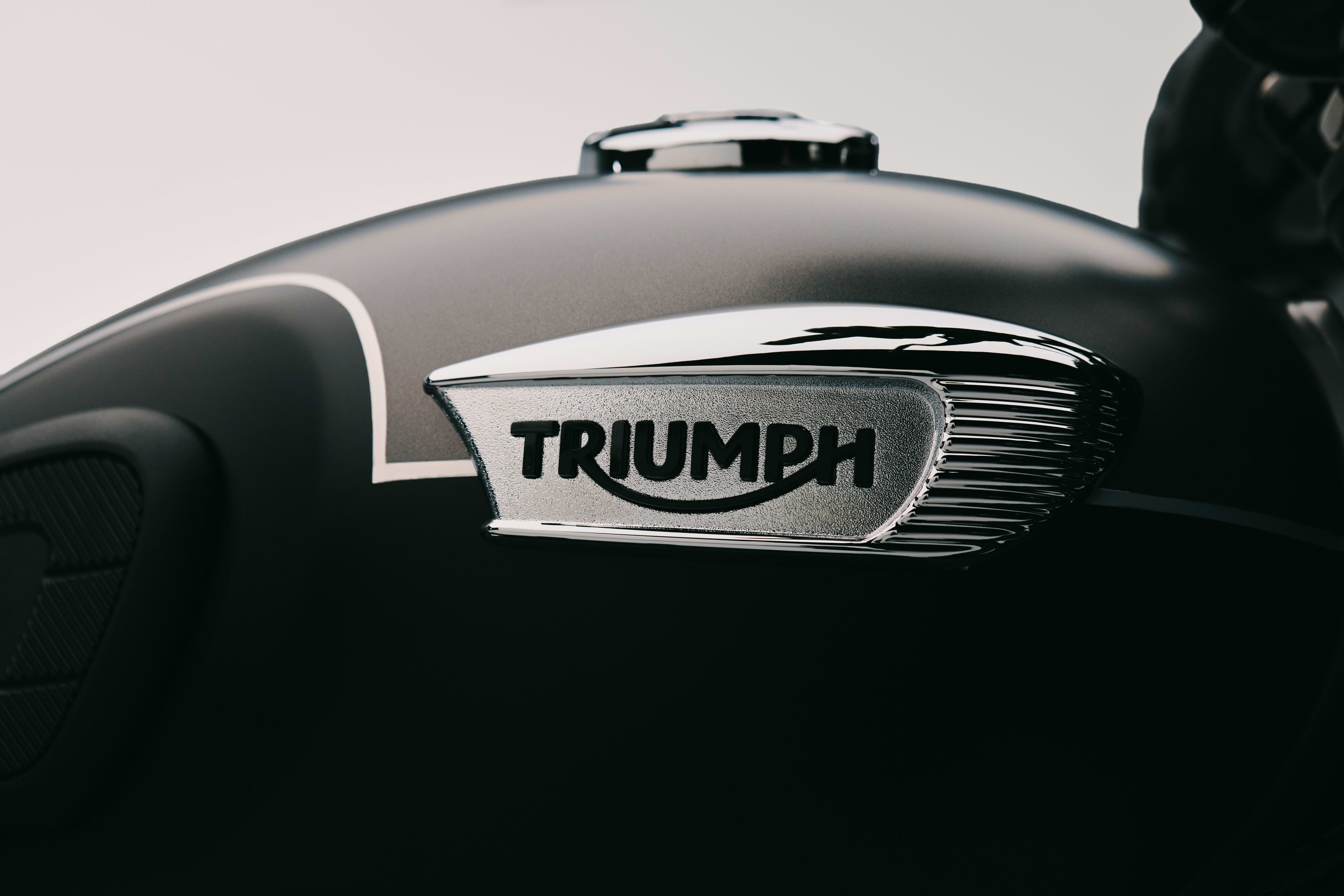 Detailed shot of a classic chrome Triumph badge on a two-tone satin grey and black Triumph Bonneville T40 Black motorcycle fuel tank.