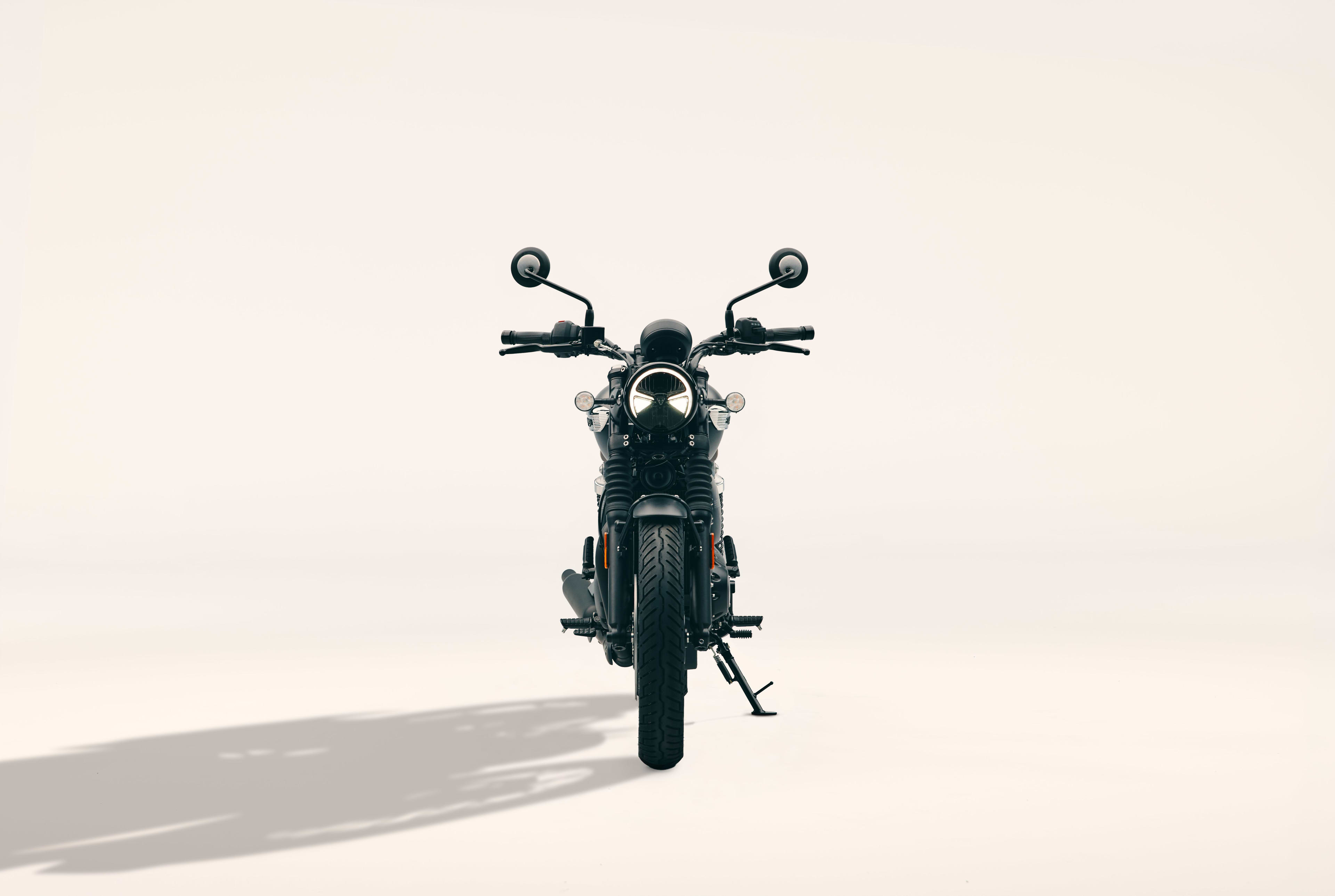 Direct front profile of a Triumph Bonneville T40 Black motorcycle with round headlight and mirrors in a studio setting.