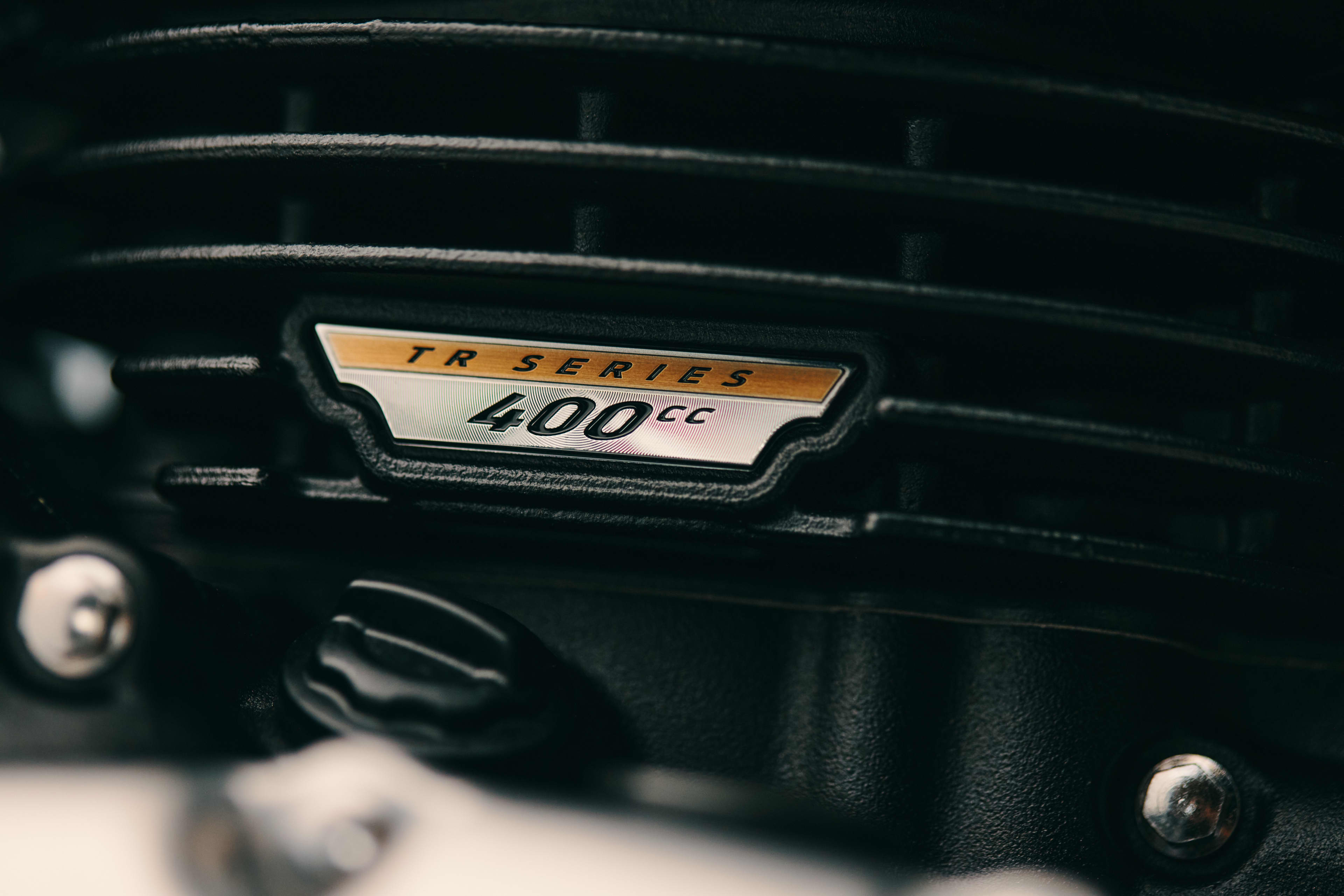Macro view of the gold and silver 'TR SERIES 400cc' emblem mounted on the cooling fins of a dark Triumph Benneville T40 engine block.