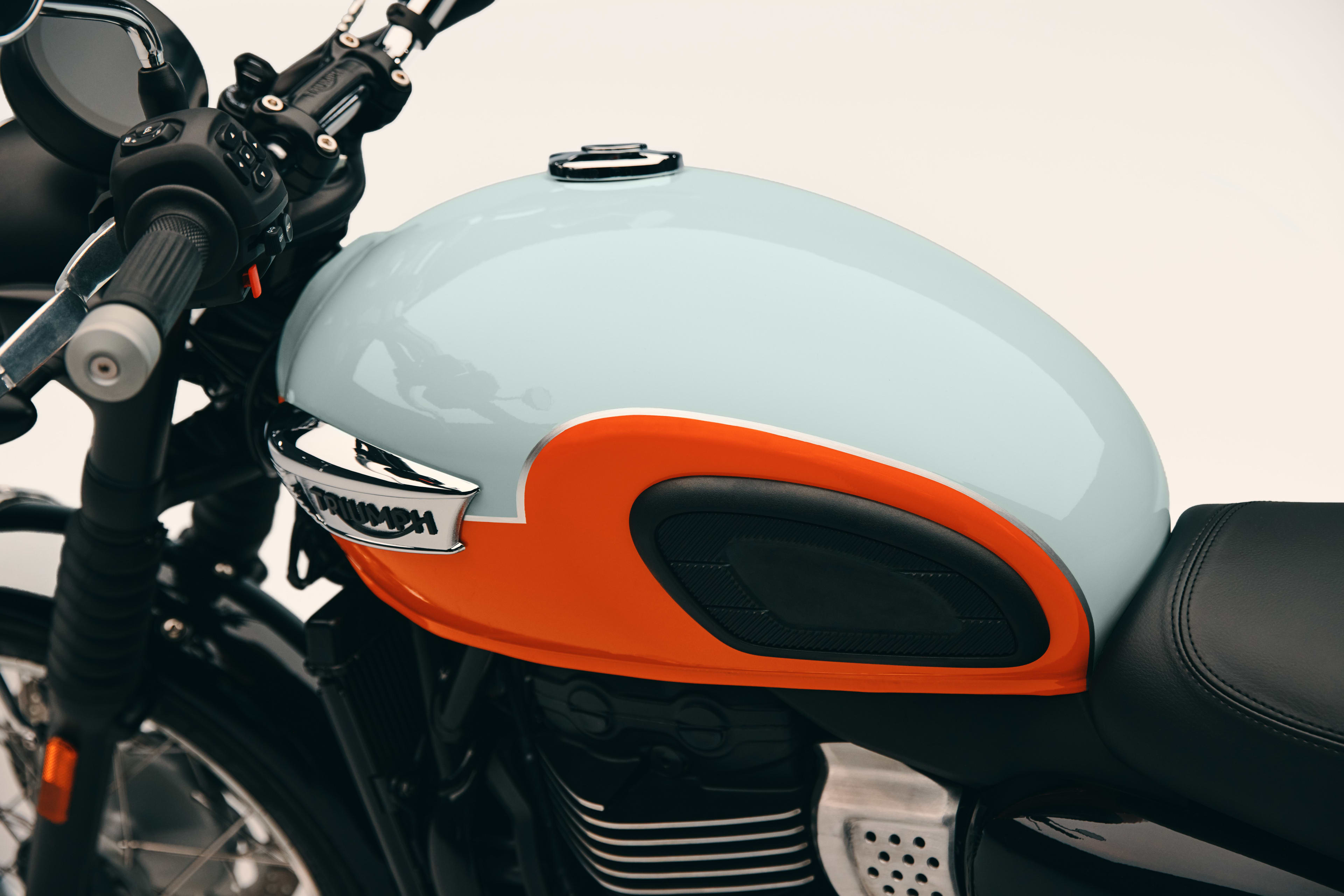 Detailed shot of a light blue and orange fuel tank with knee pads and chrome badge on a Triumph Bonneville T40 motorcycle.