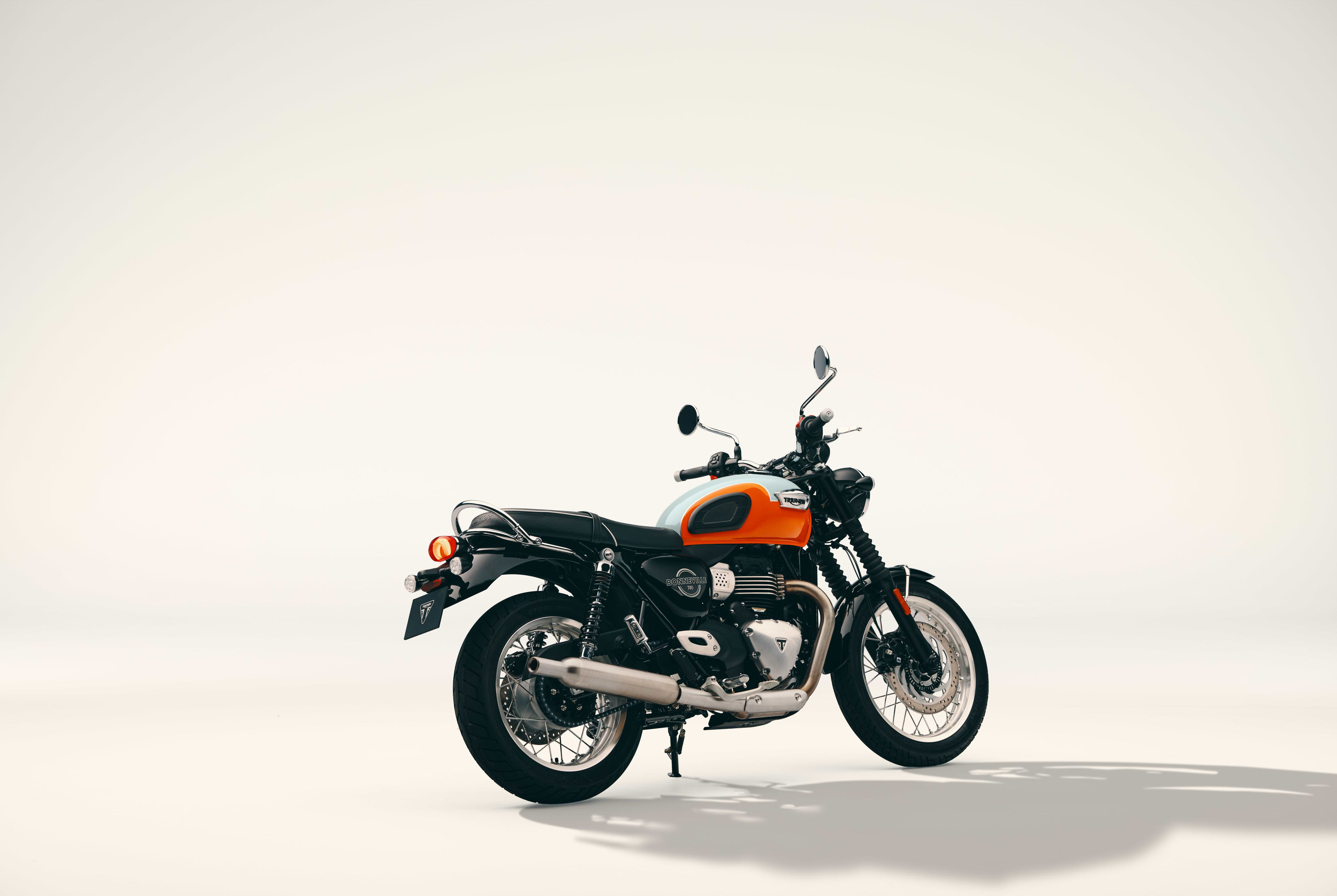 Rear three-quarter studio shot of a Triumph Bonneville T40 motorcycle with an orange and white tank on a light background.
