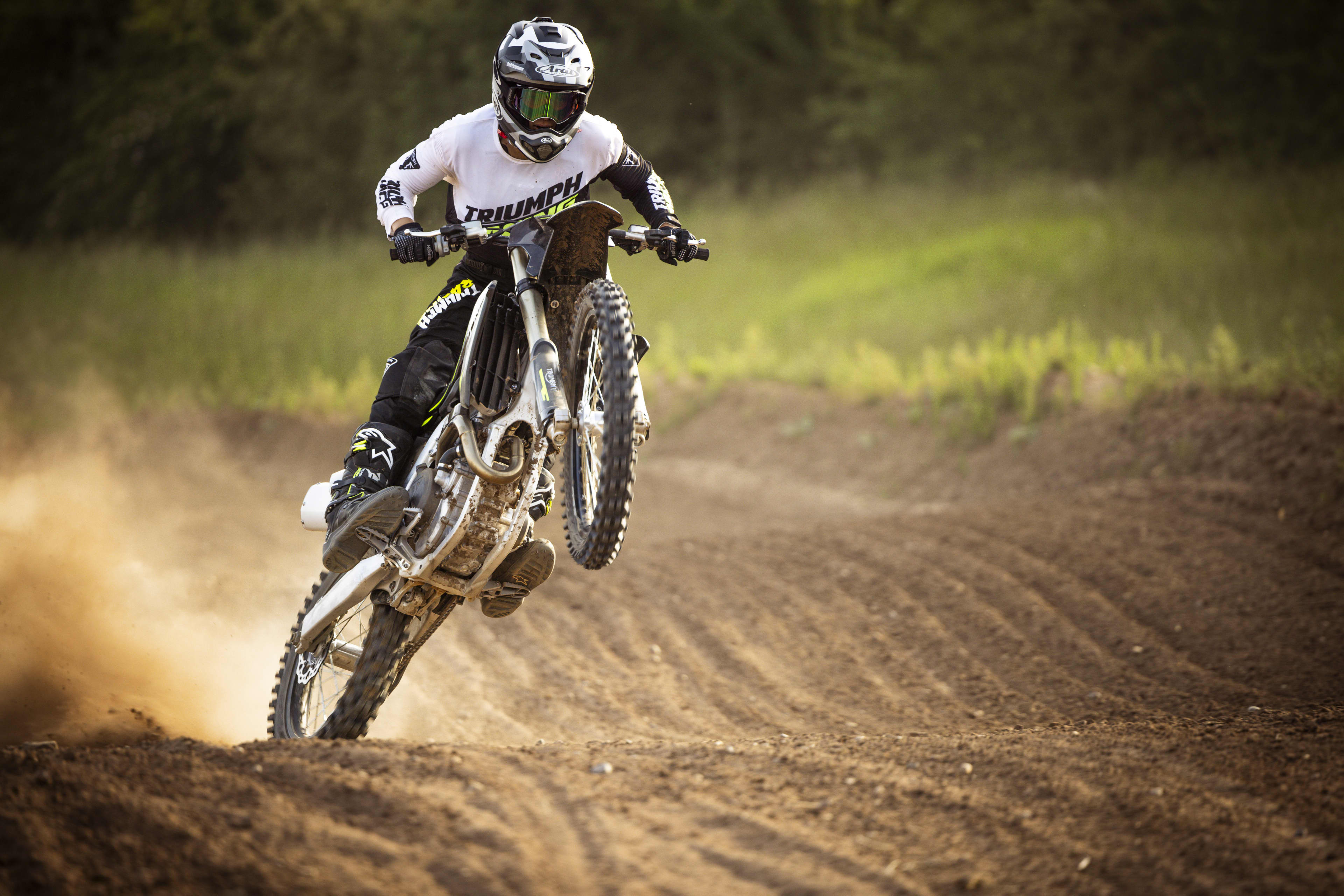 A rider popping a wheelie on a Triumph 250-X motocross bike along a dirt track.