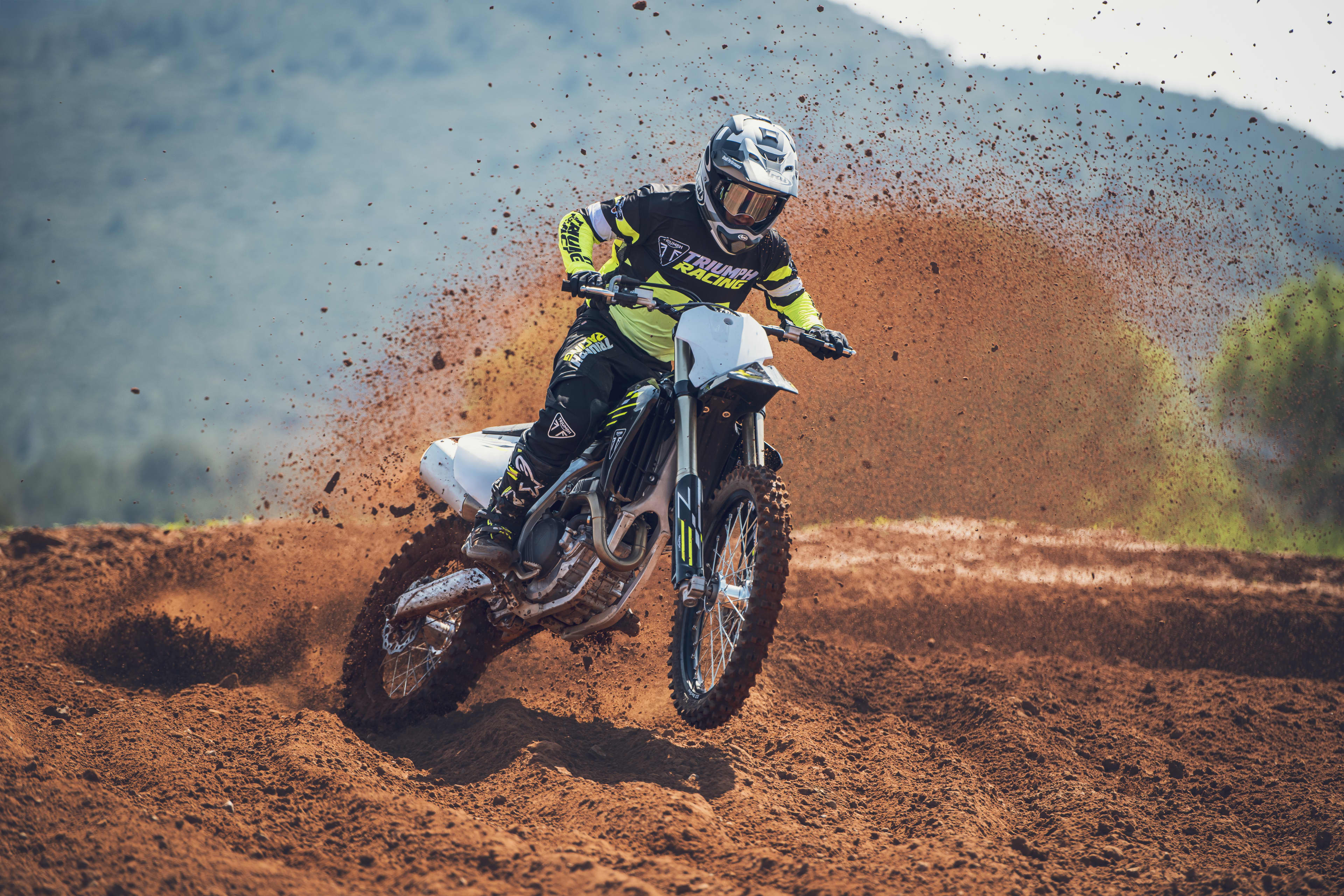 Triumph TF 250-X (MY26) front angle with rider on red dirt spraying mud from back wheel