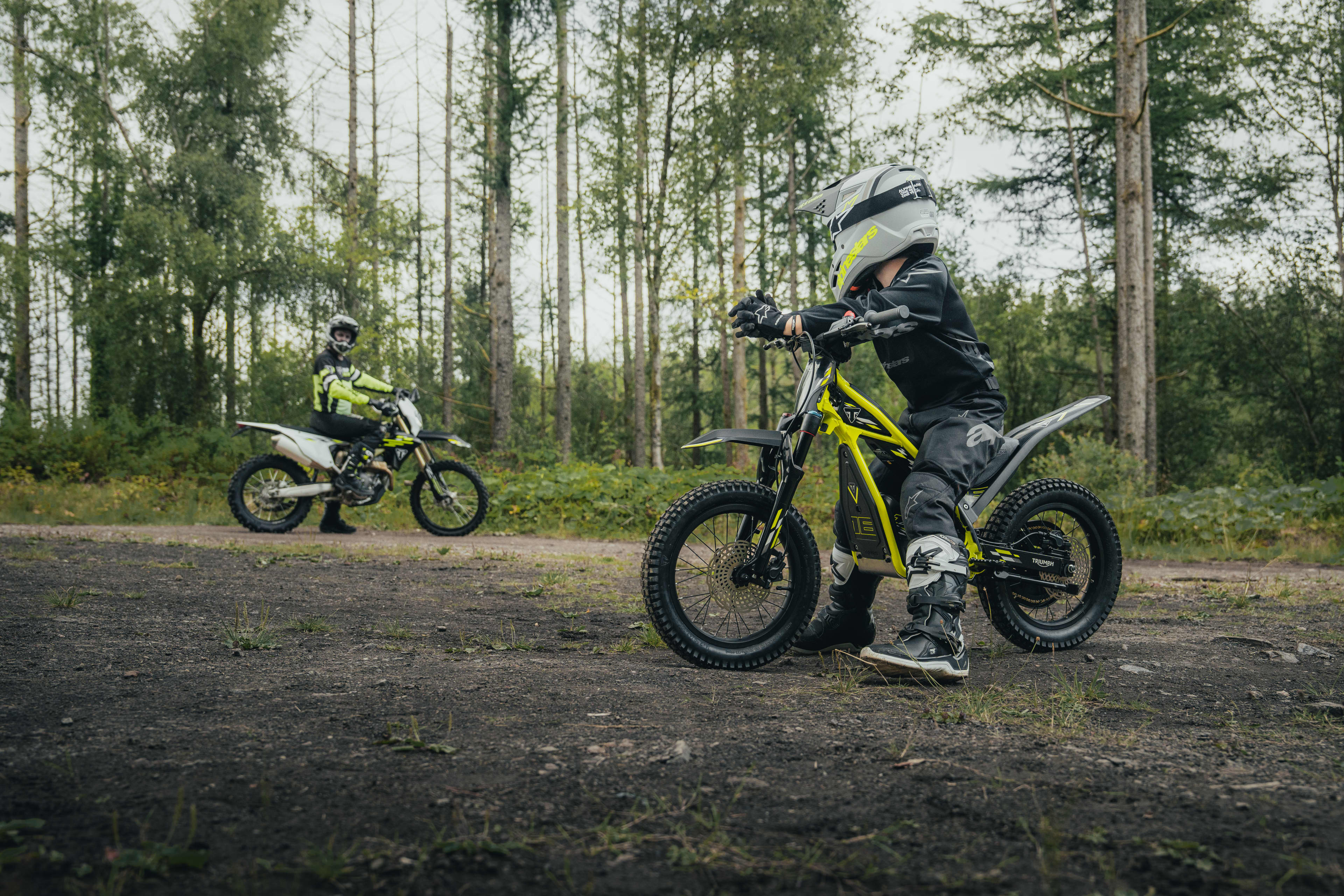 Young riders out riding on the Triumph TXP-16 in a forest with an adult supervision.