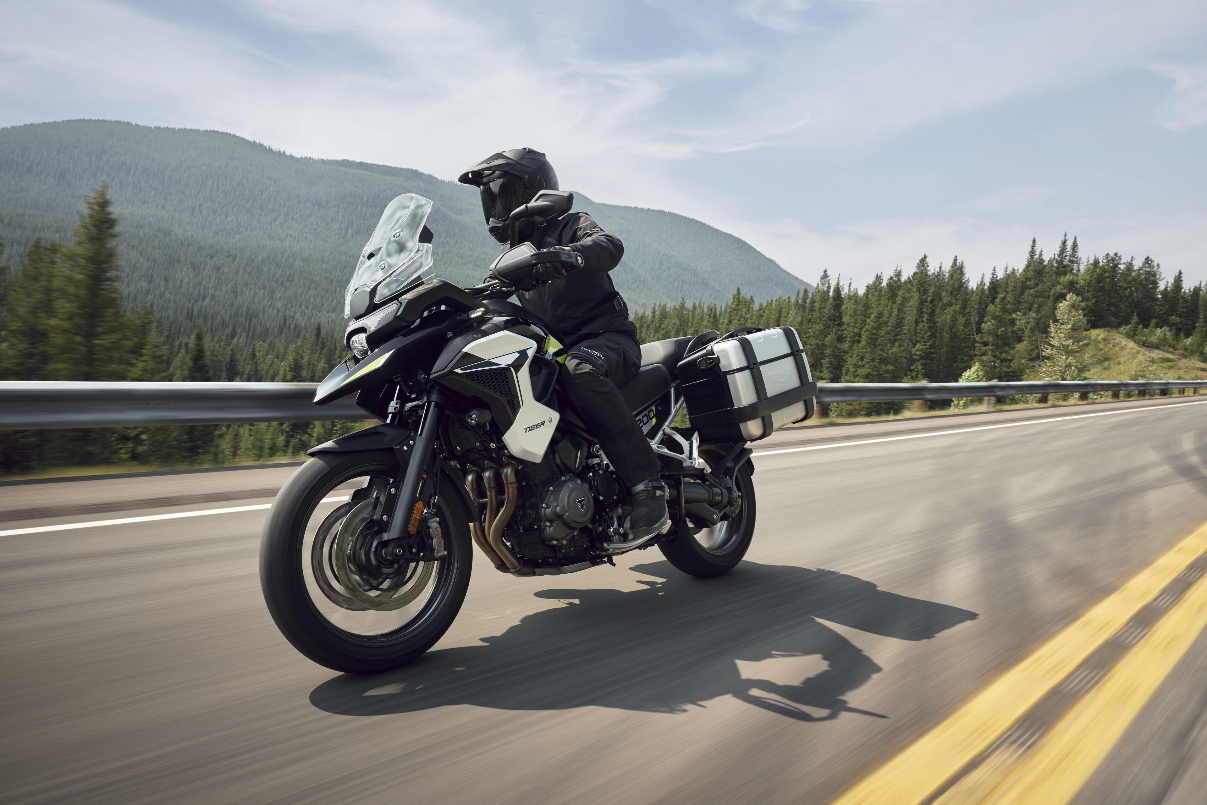 Action shot of a rider on a Triumph Tiger 1200 GT Pro with side panniers riding along an open mountain highway.