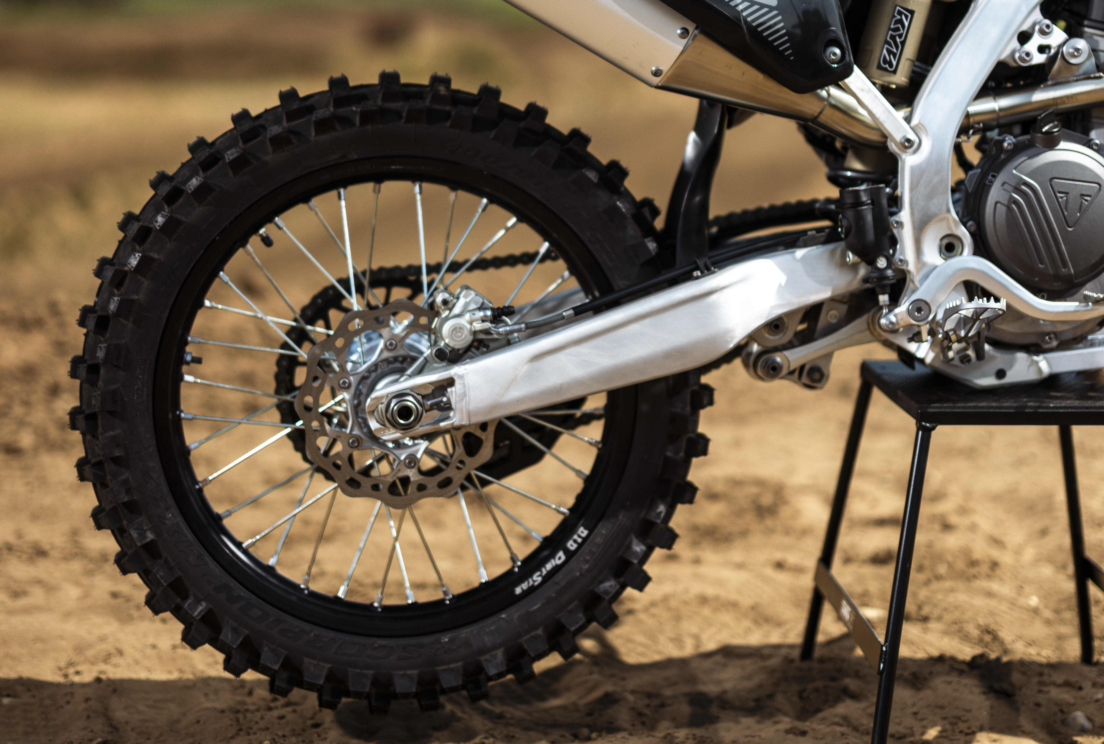 Side profile shot of the rear assembly of a Triumph TF 250-X motocross bike resting on a stand, showing the knobby rear tyre, DID DirtStar rim, swingarm and rear brake disc.
