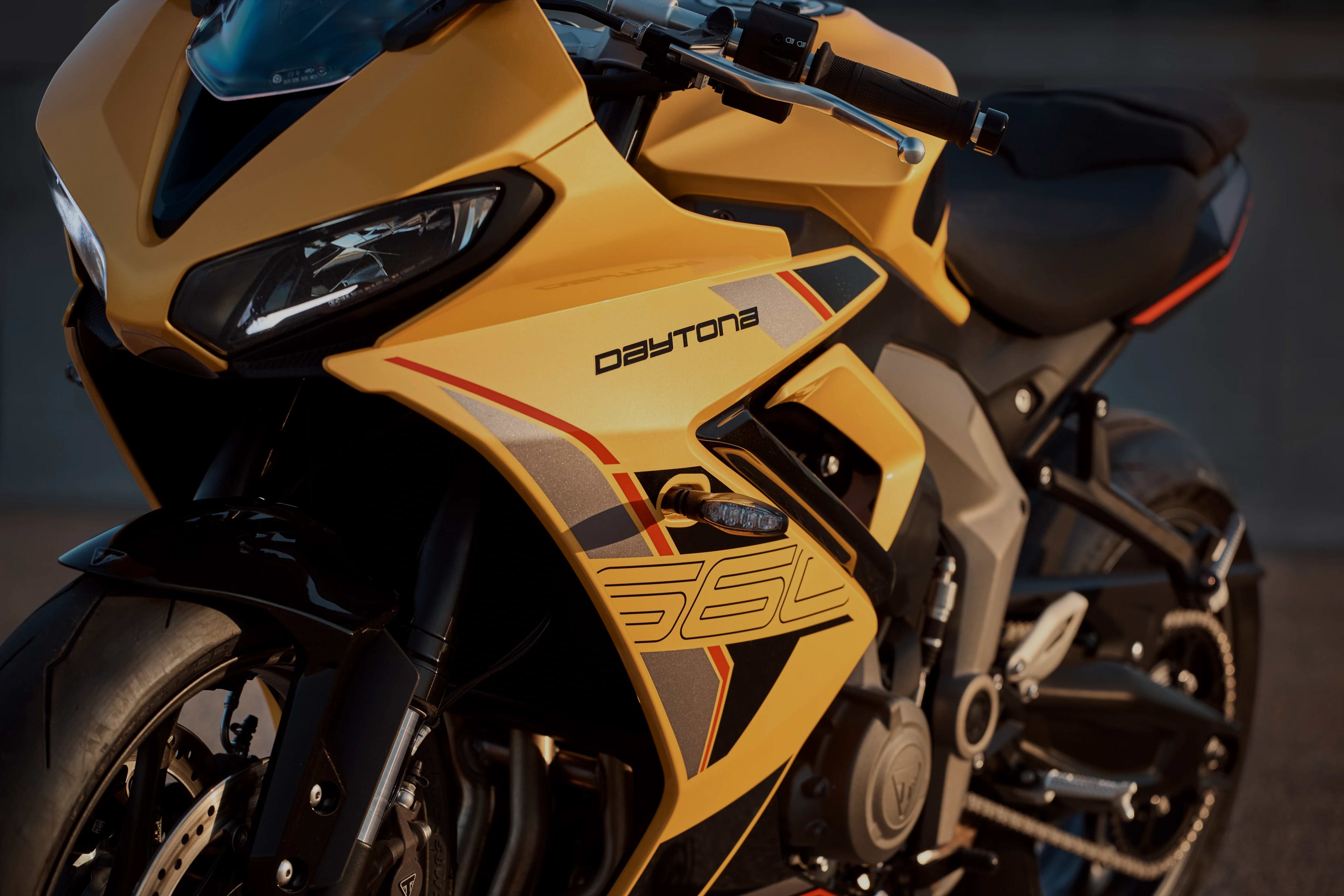 Black and silver Triumph Speed Triple RS with yellow accents, parked beside a ribbed wall.