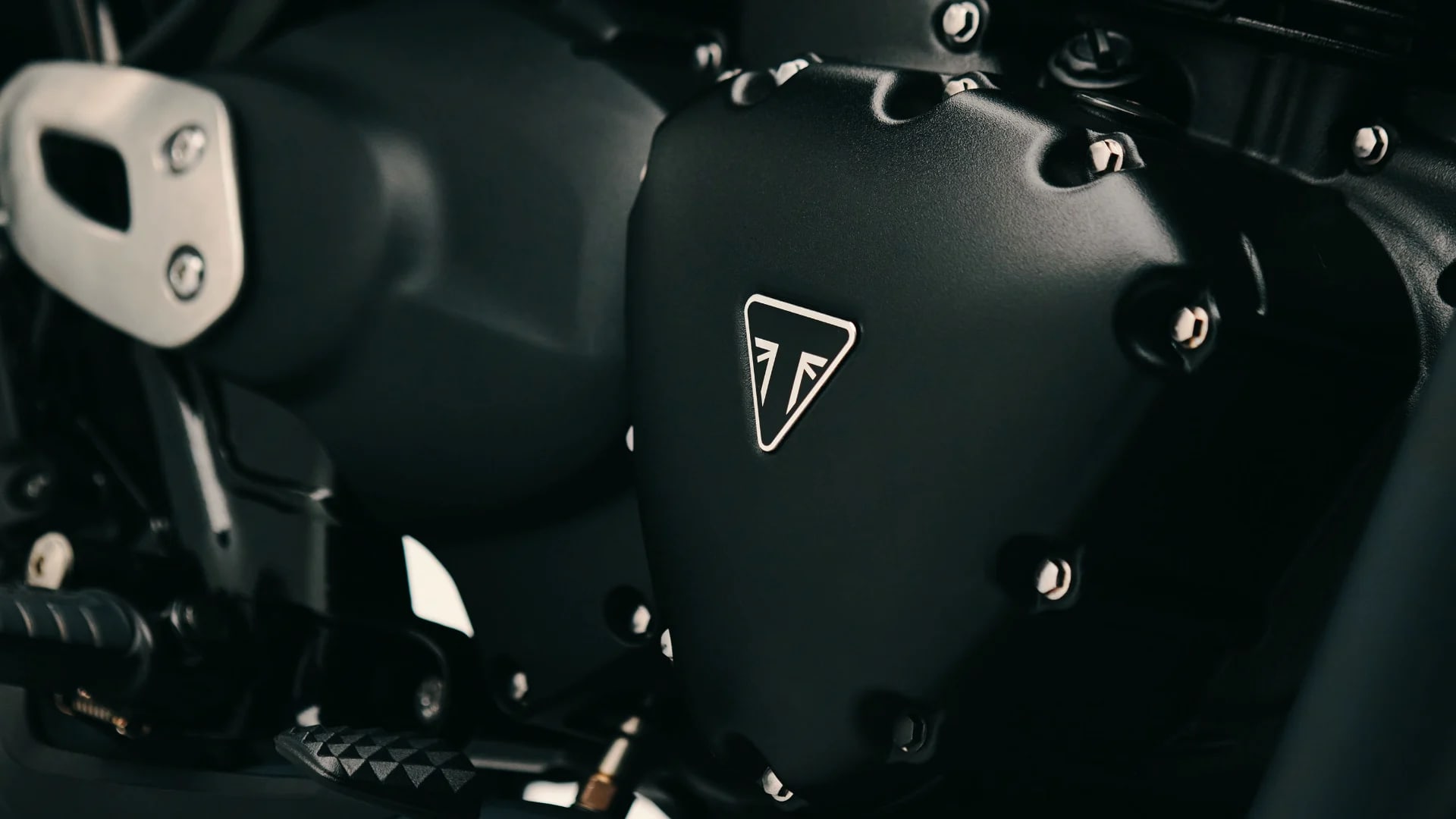 Detailed macro shot of a powder coated black engine casing featuring the white triangular Triumph logo on the Bonneville T40 Black.
