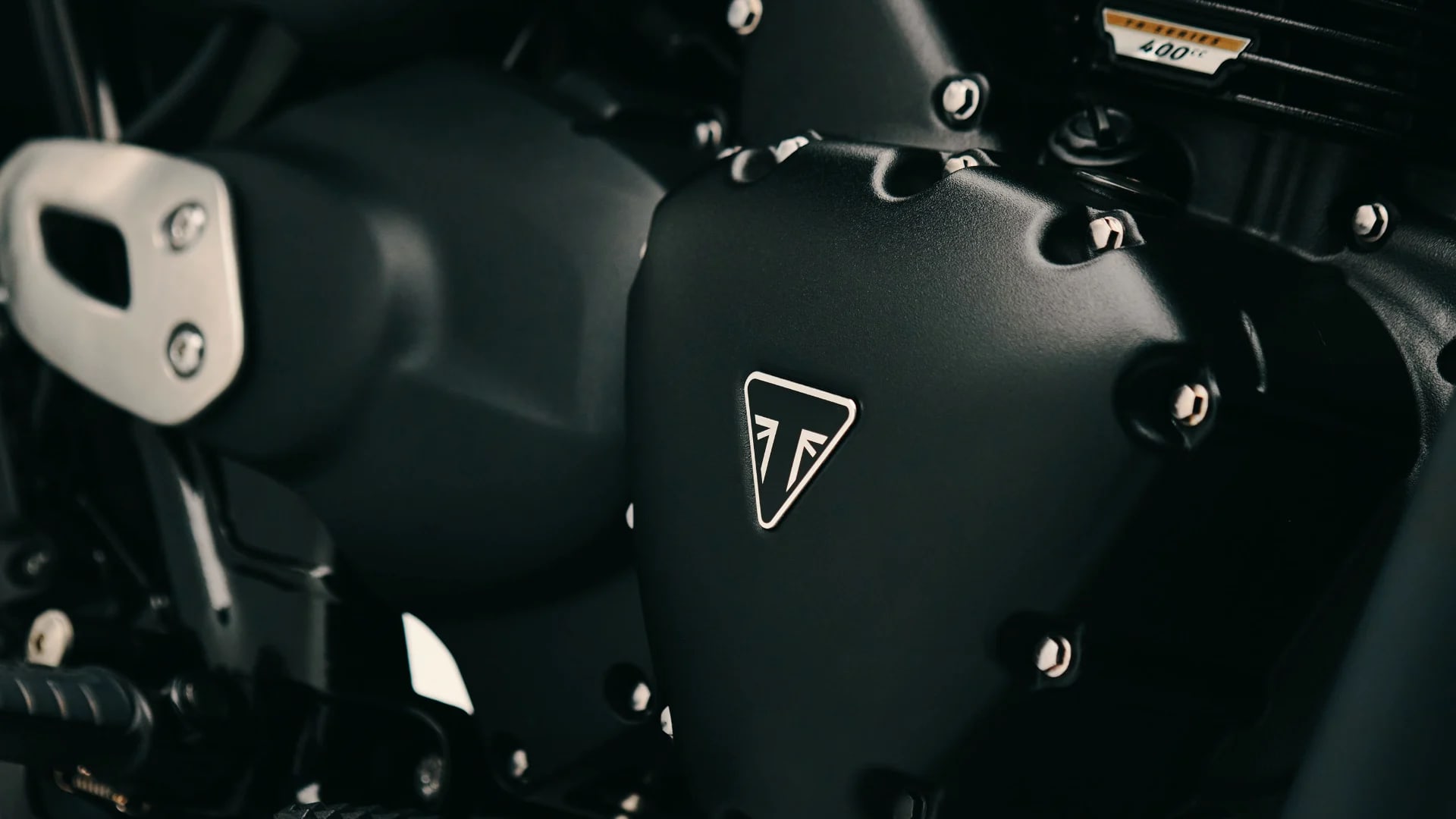 Detailed macro shot of a powder coated black engine casing featuring the white triangular Triumph logo on the Bonneville T40 Black.
