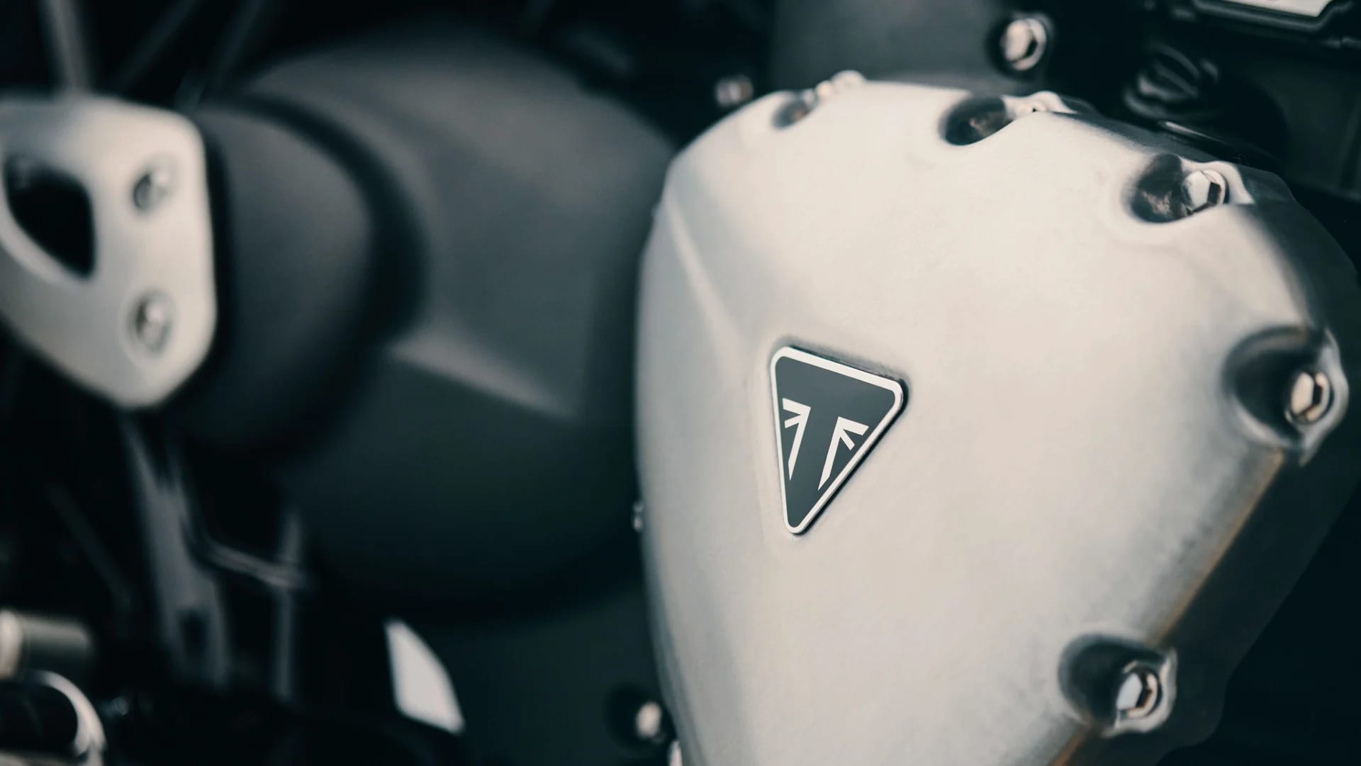 Detailed macro shot of a brushed aluminum engine casing featuring the black triangular Triumph logo on the Bonneville T40.