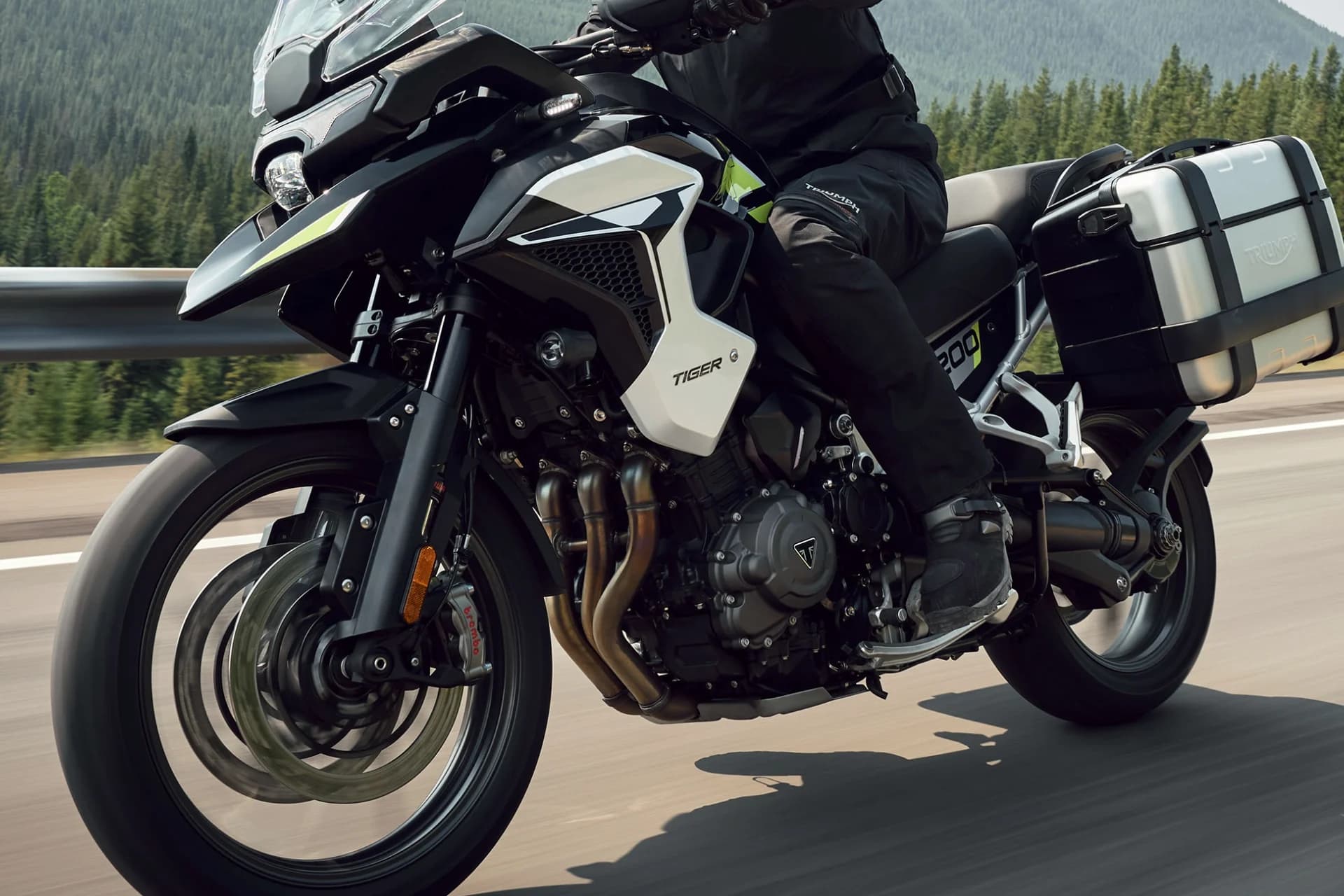 Front three-quarter close-up action shot of a Triumph Tiger 1200 GT Pro riding along a paved road.
