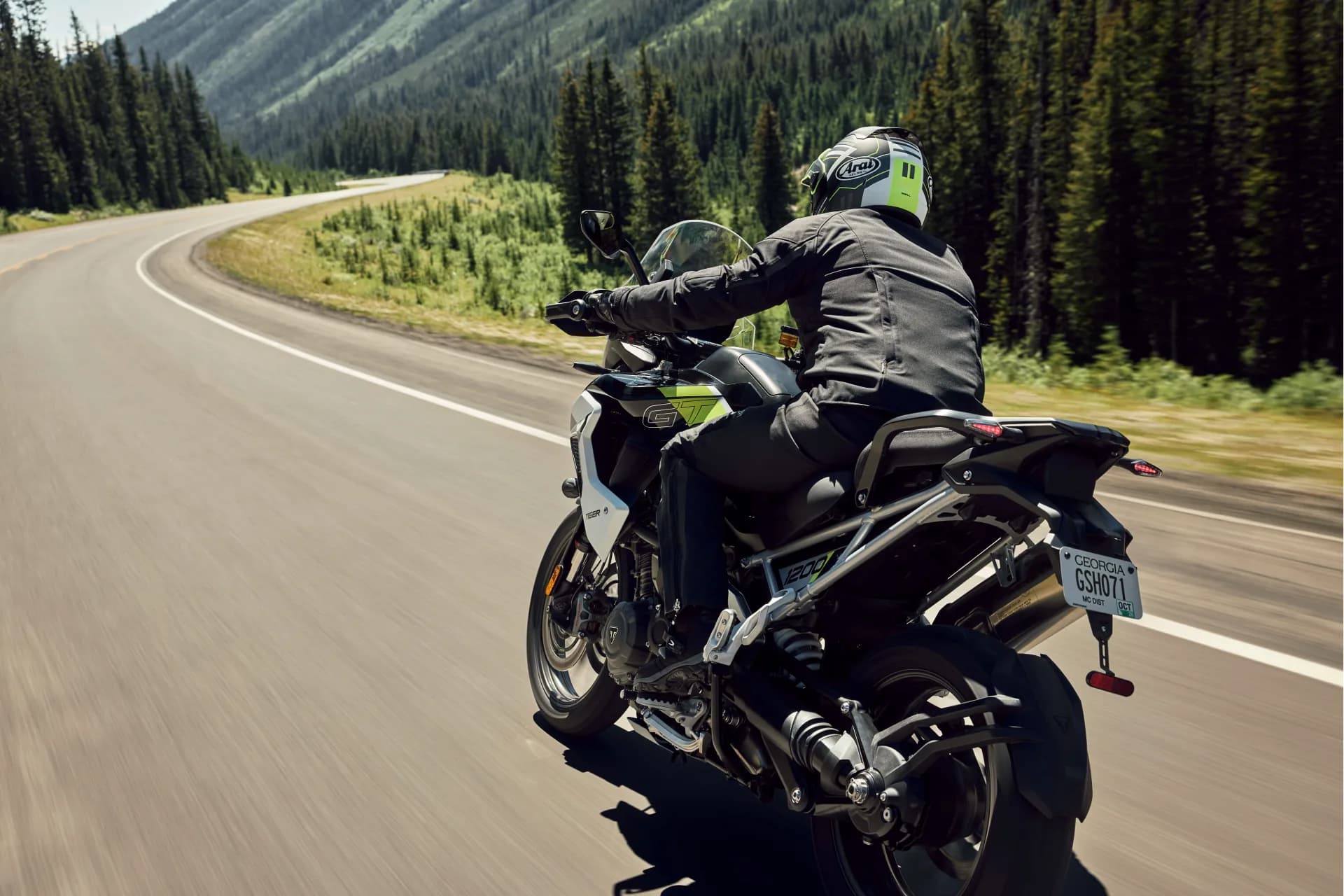 Action rear three-quarter view of a motorcyclist riding a Triumph Tiger 1200 GT Pro along a scenic winding mountain road.