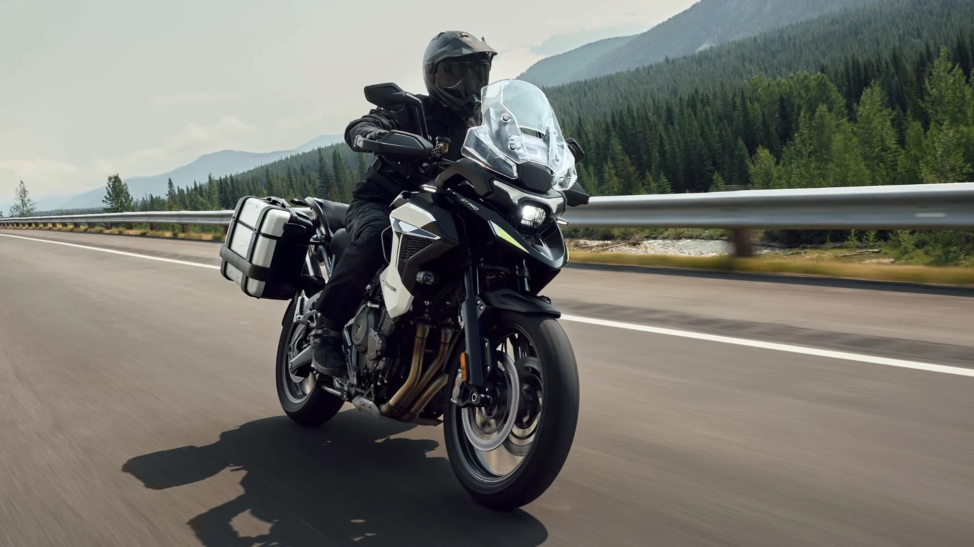 Front three-quarter action shot of a rider on a Triumph Tiger 1200 GT Pro equipped with hard luggage panniers on a highway.