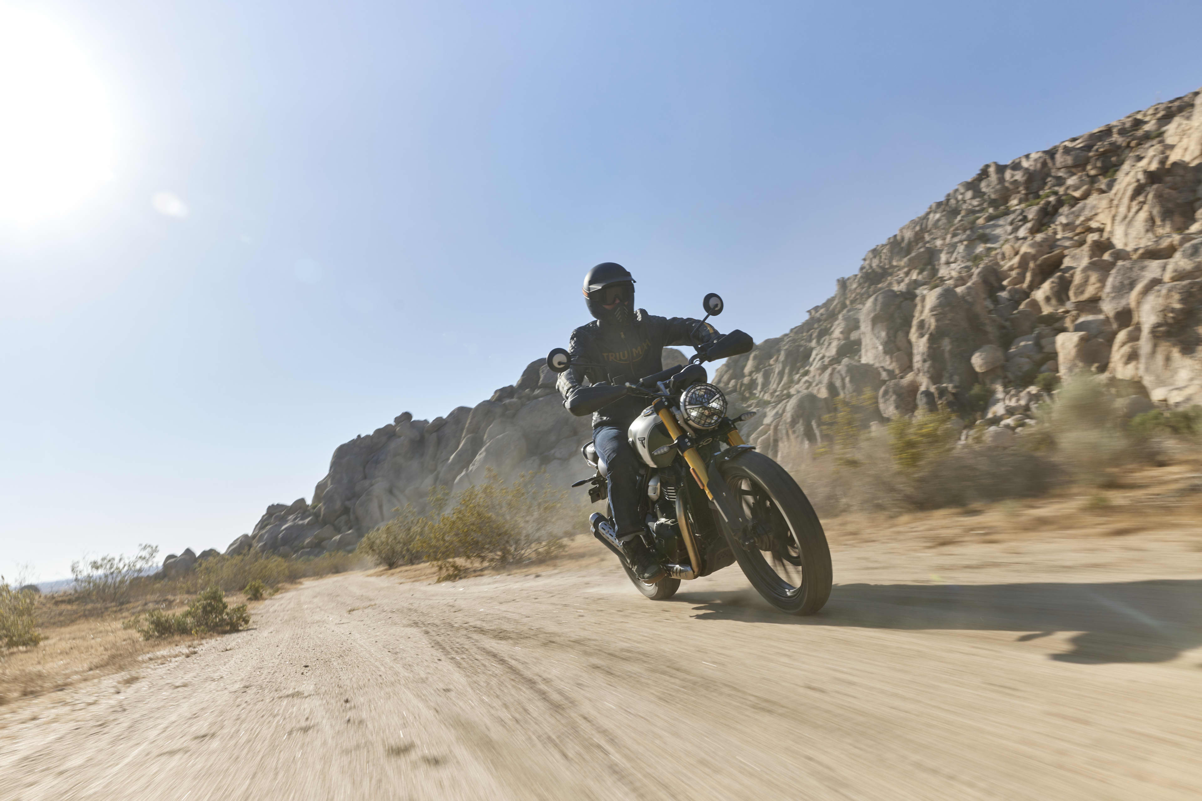 Triumph Scrambler 400 X with rider on a sandy road in the sun