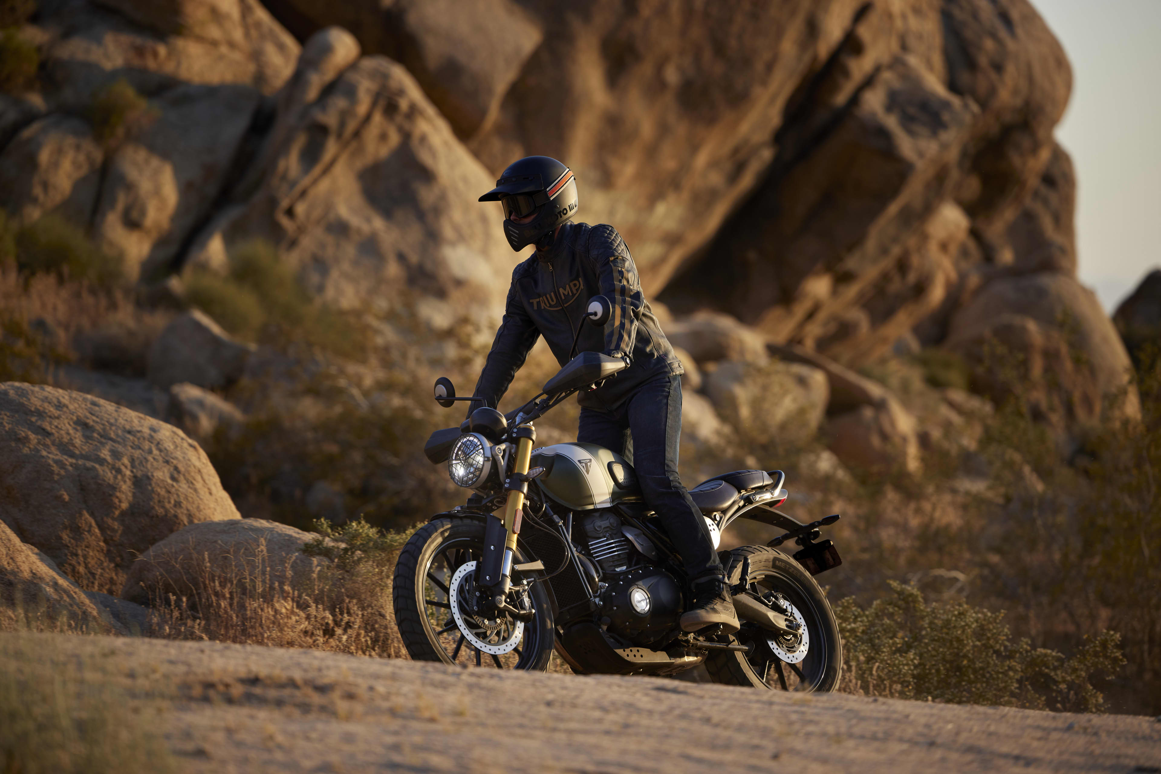 Rider on a Triumph Scrambler 400 X in front of large boulders