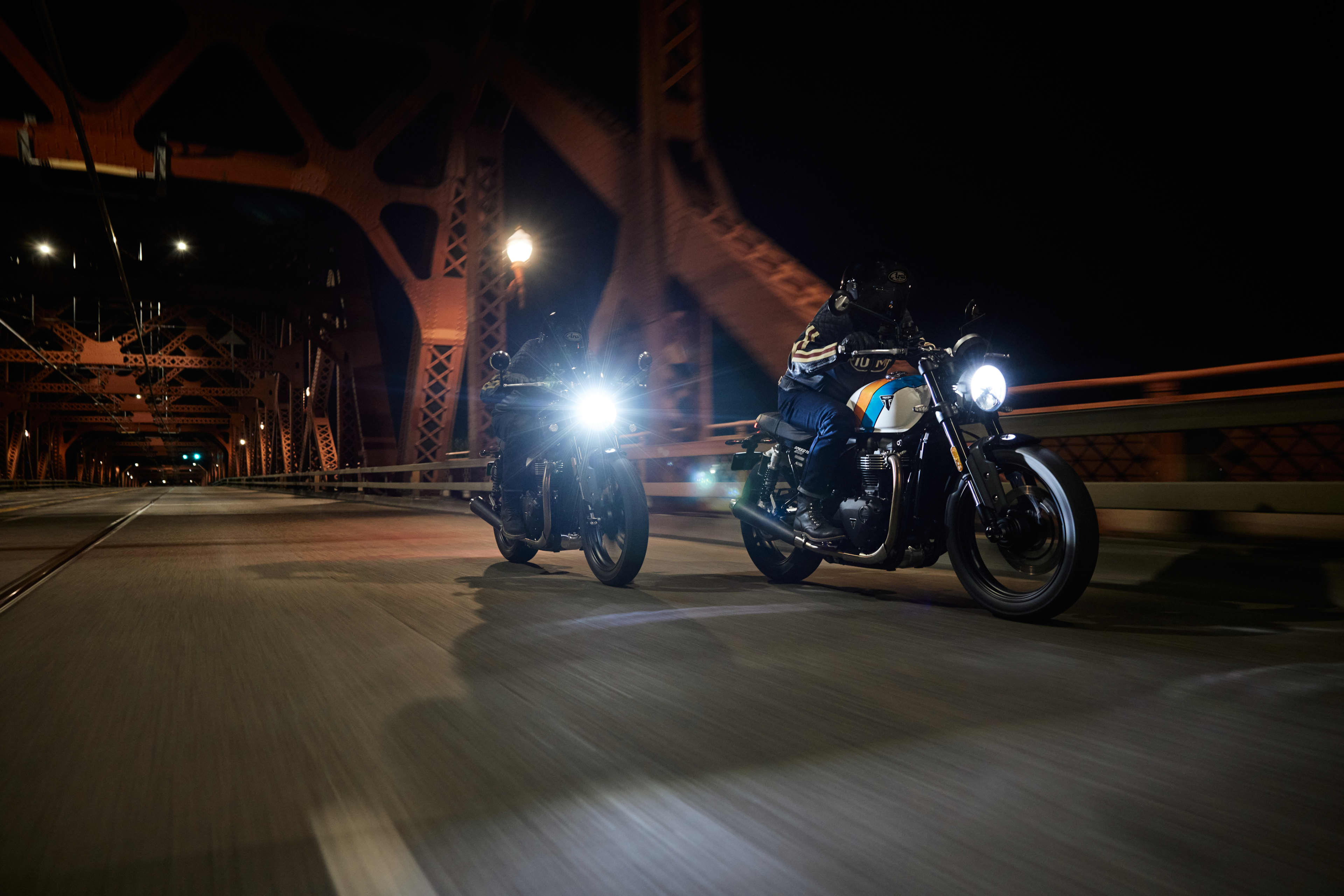 Angled front view action shot of two riders on Triumph Speed Twin 900 crossing a bridge